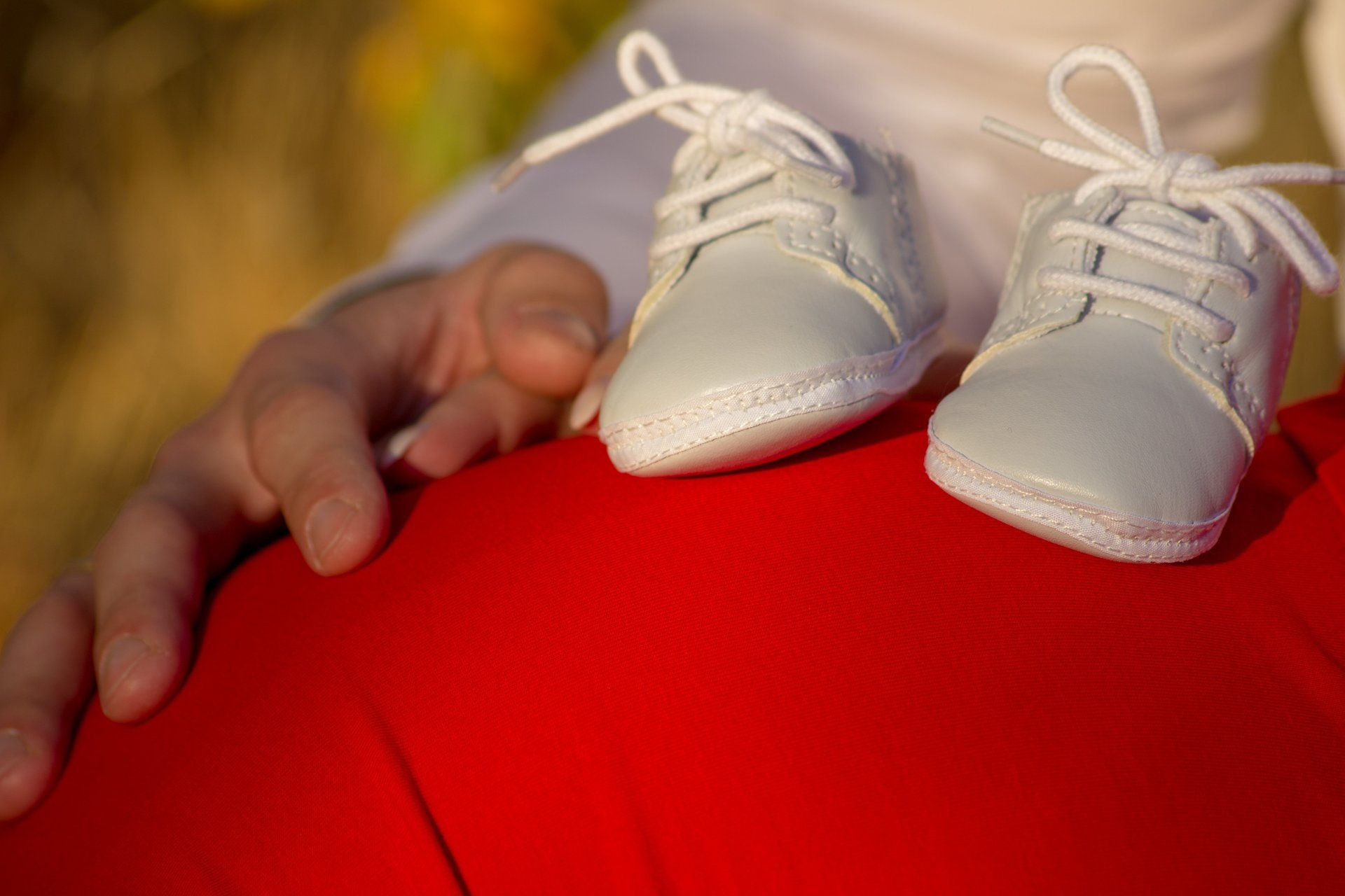 Babybauch in rotem Kleid mit weißen Babyschüchen und der Hand vom Papa auf dem Bauch