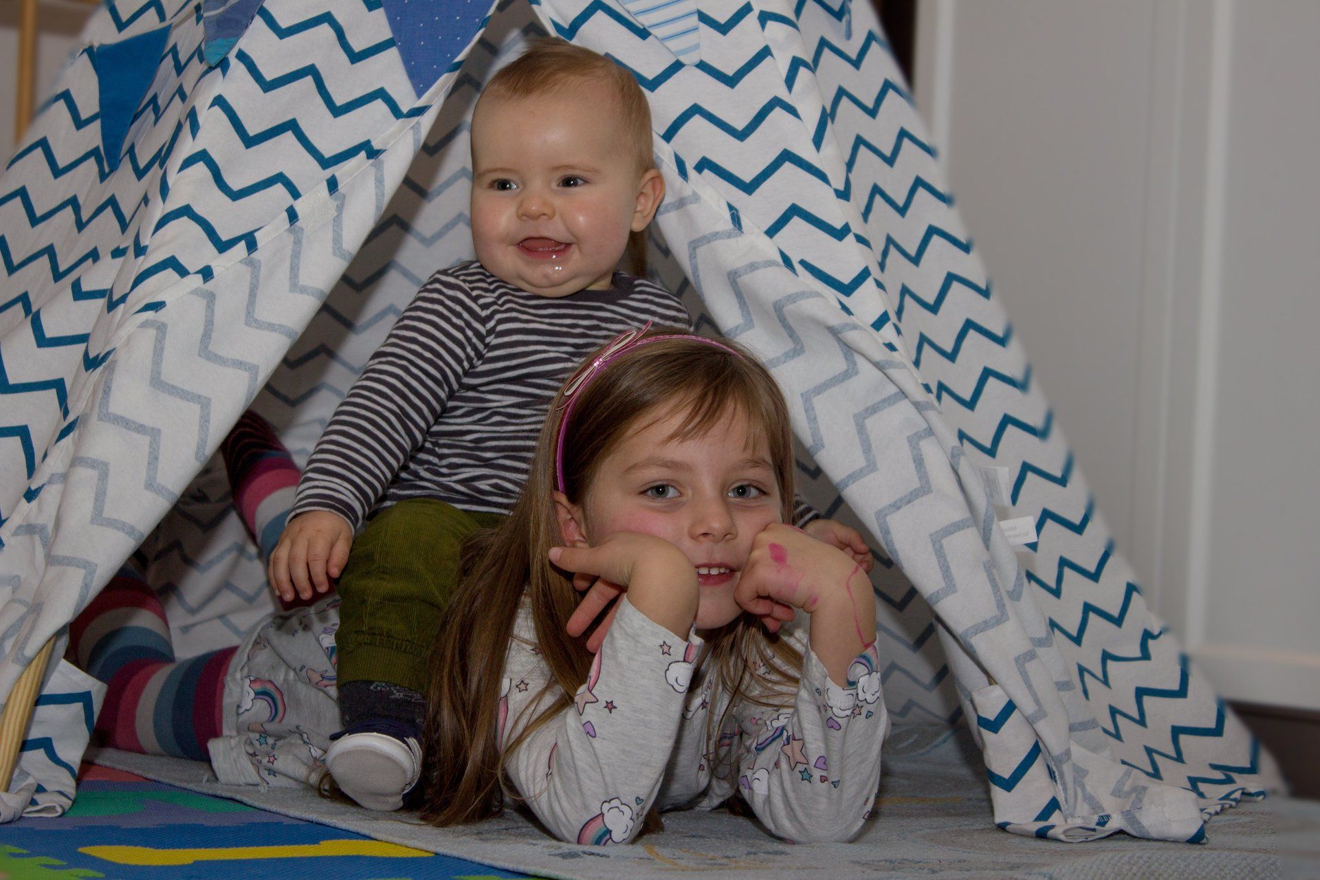 Geschwisterpaar vorm Indianerzelt, Mädchen auf Bauch liegend und kleiner Bruder auf ihrem Rücken sitzend