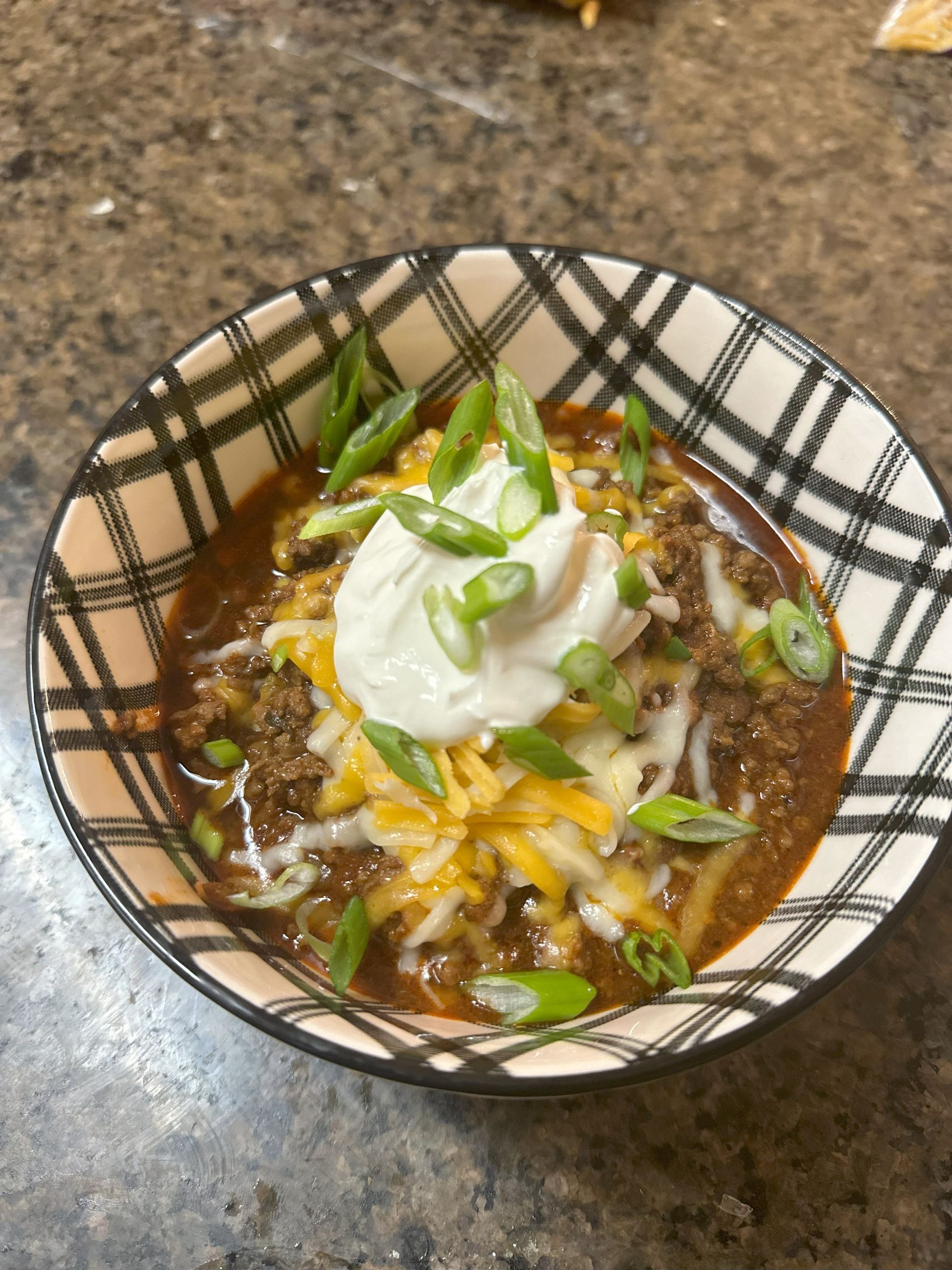 homemade bowl of chili topped with cheese, sour cream and sliced green onions.