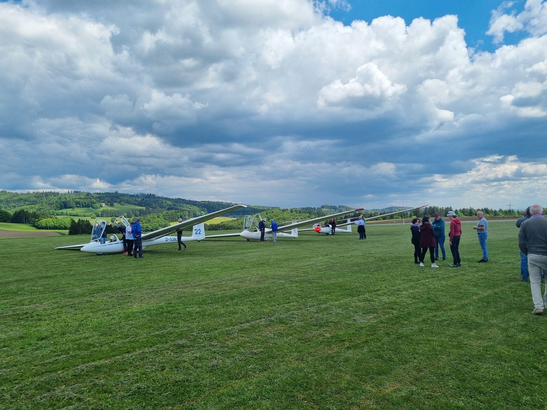 Drei Doppelsitzer im Einsatz beim Schnupperflugtag der LGH Drei doppelsitzige Segelflugzeuge stehen auf einer Wiese, jeweils Leute am Flugzeug, am Himmel eindrucksvolle Cumulusbewölkung.