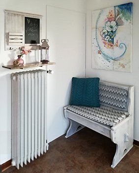 Blick in den Flur, durch den Sie die Ferienwohnung betreten. Rechts eine gemütliche Truhenbank. Darüber ein Bild er Künstlerin Annadoria. Geradeaus eine kleine Ablage für Schlüssel etc. Darüber ein Infoboard aus Holz mit Schiefertafel und Haken.