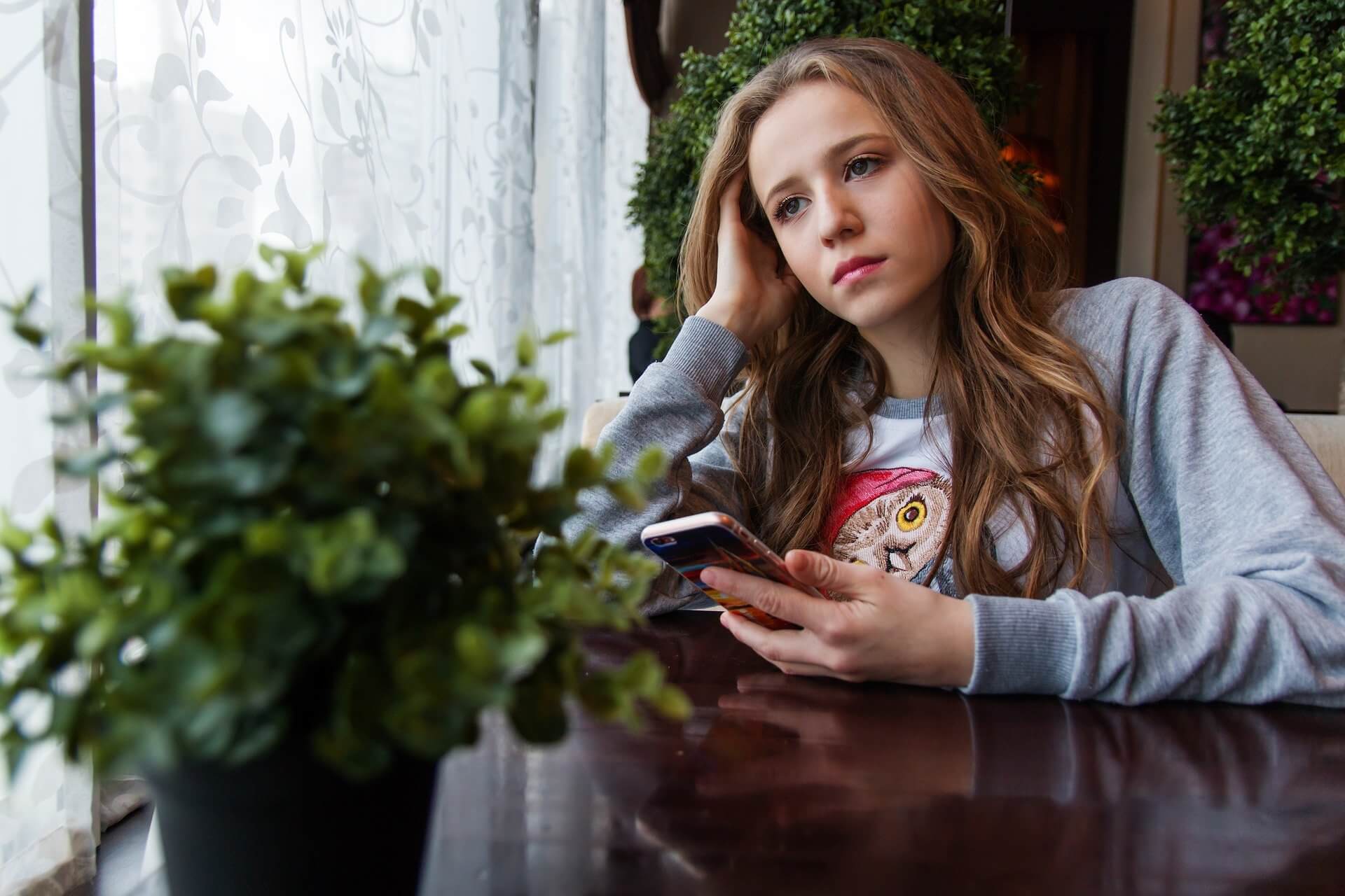 Social Media und Depression: trauriges Mädchen sitzt mit einem Smartphone am Tisch