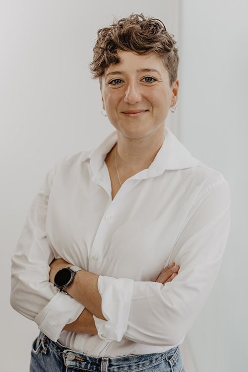 Steffi Müsse, eine Frau mit blauem Blazer und Hemd, sitzt an einem Tisch. Sie schaut in einen Laptop vor sich und hat ein Handy in der Hand