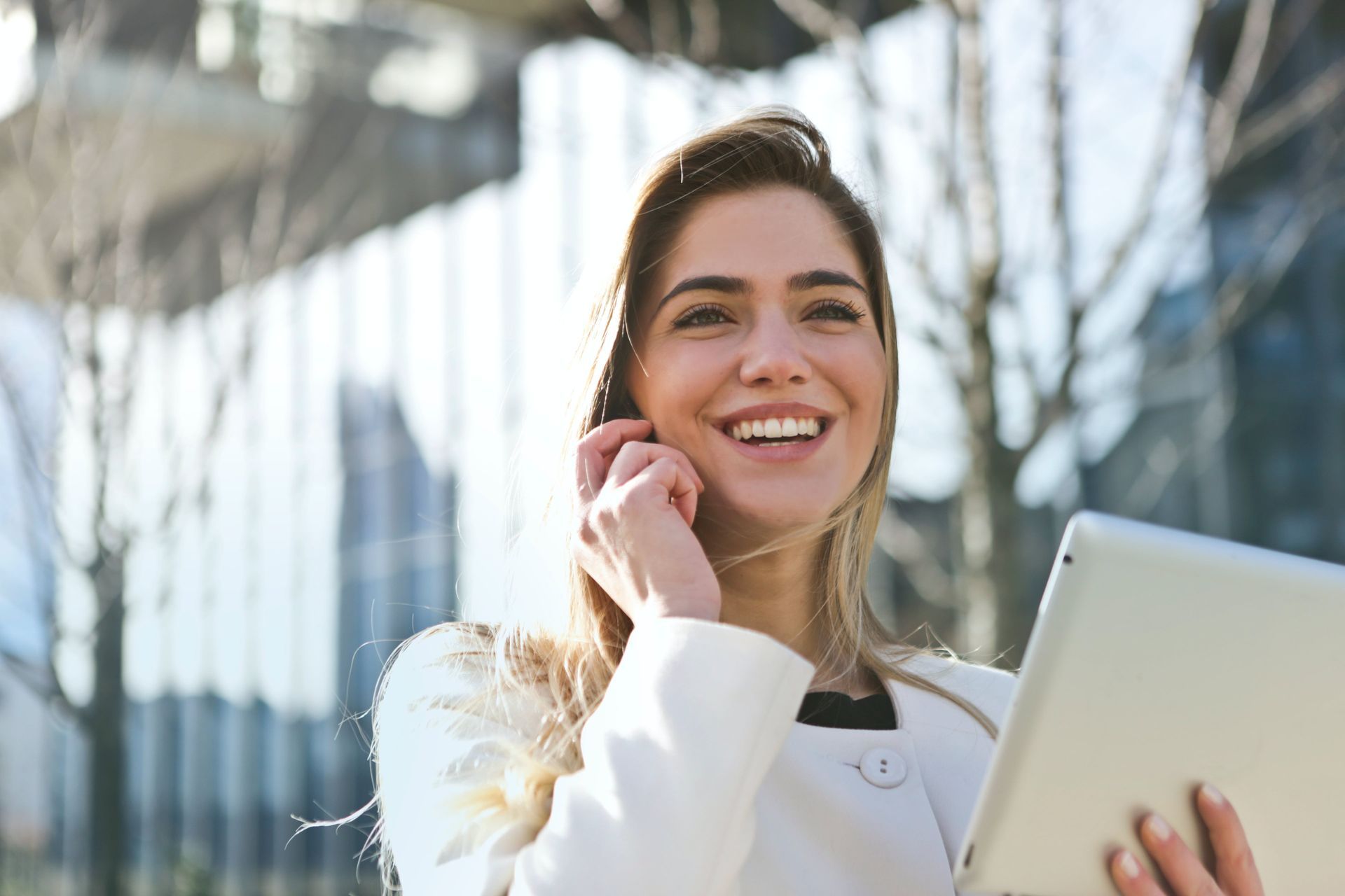 A woman smiling in front of an office building while calling a friend