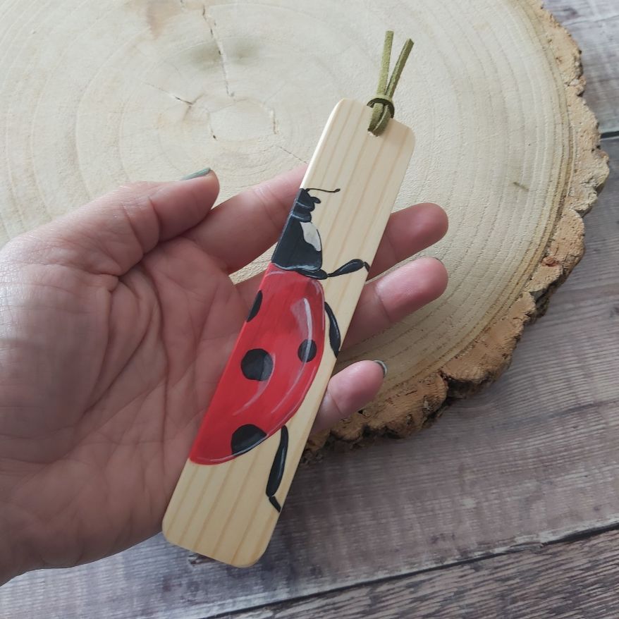 Hand holding bookmark with a ladybird painted on it