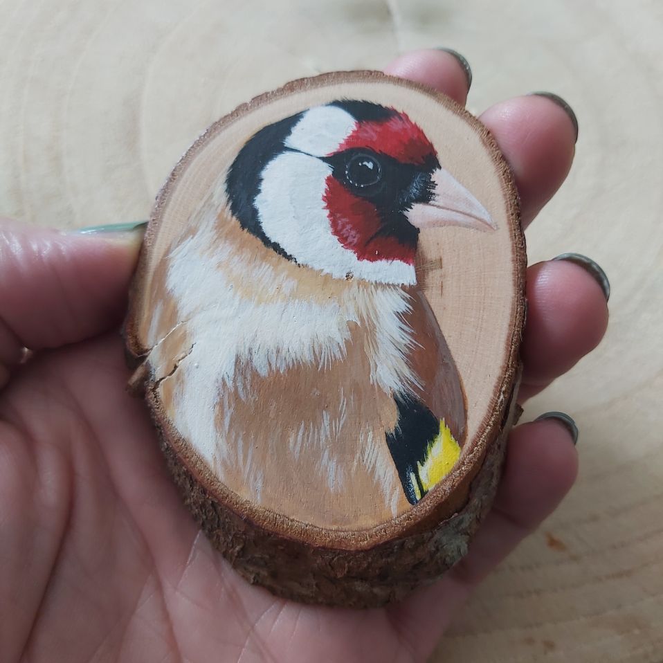 Hand holding a wood slice painted with a goldfinch