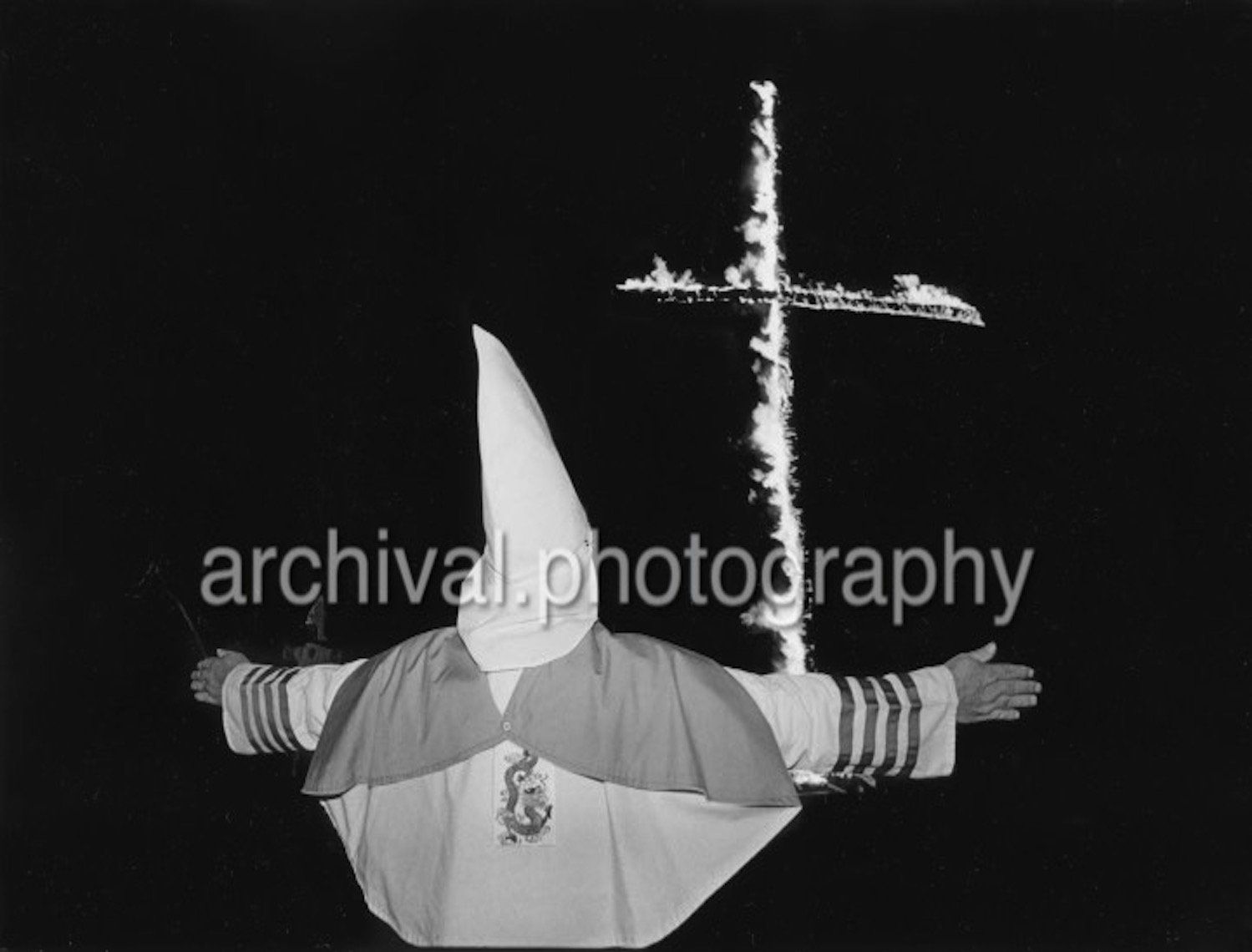 KKK member with cross burning in background