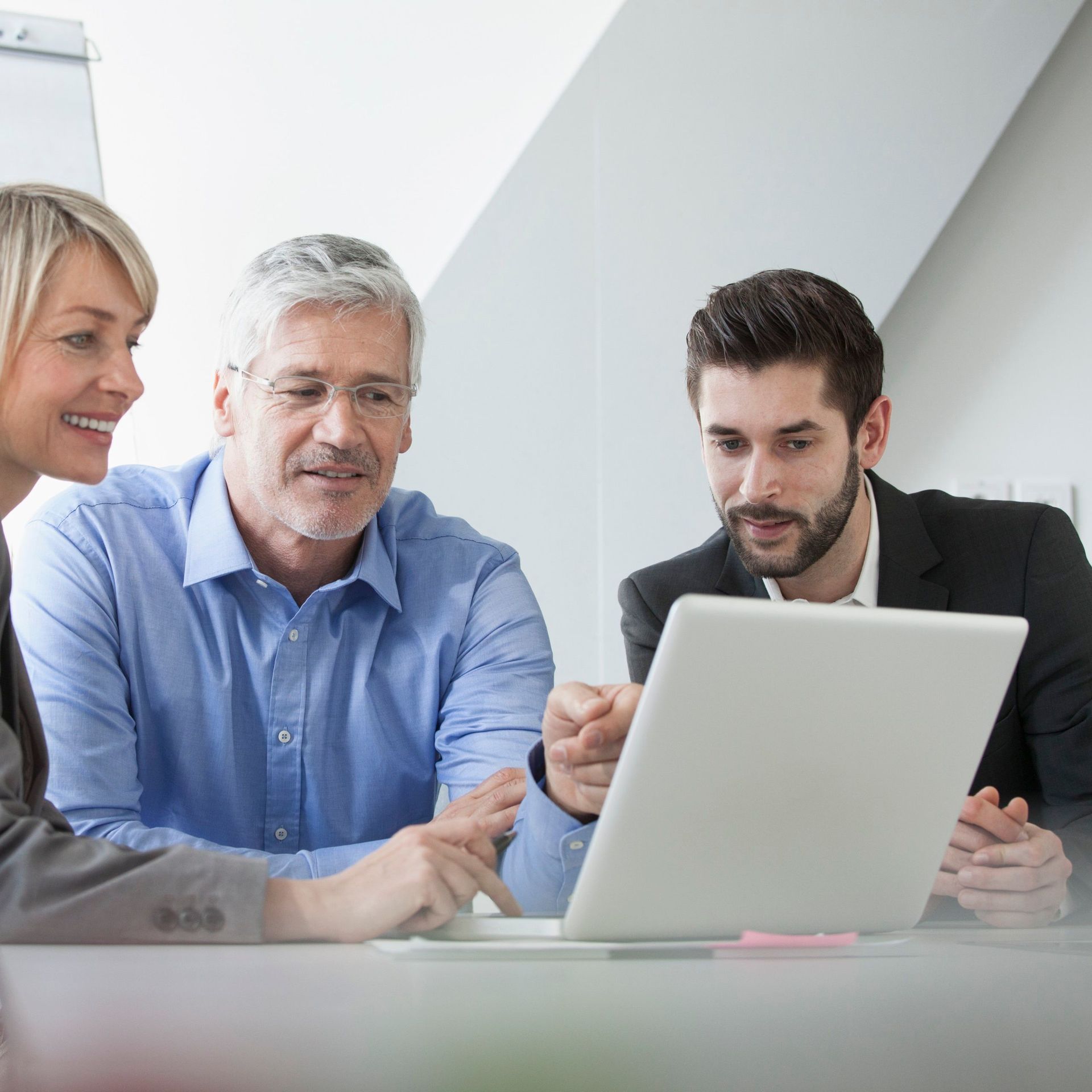 3 Mitarbeiter, welche sich sehr interessiert etwas auf ihrem Laptop anschauen