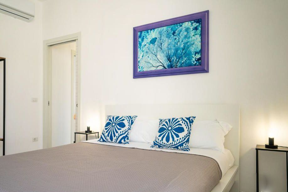 Letto matrimoniale, cusini azzurri sopra il letto e quadro azzurro appeso alla parete.