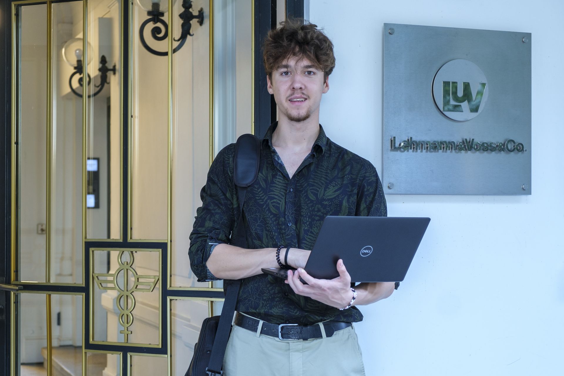 Artem steht mit Laptop vor Firmenschild
