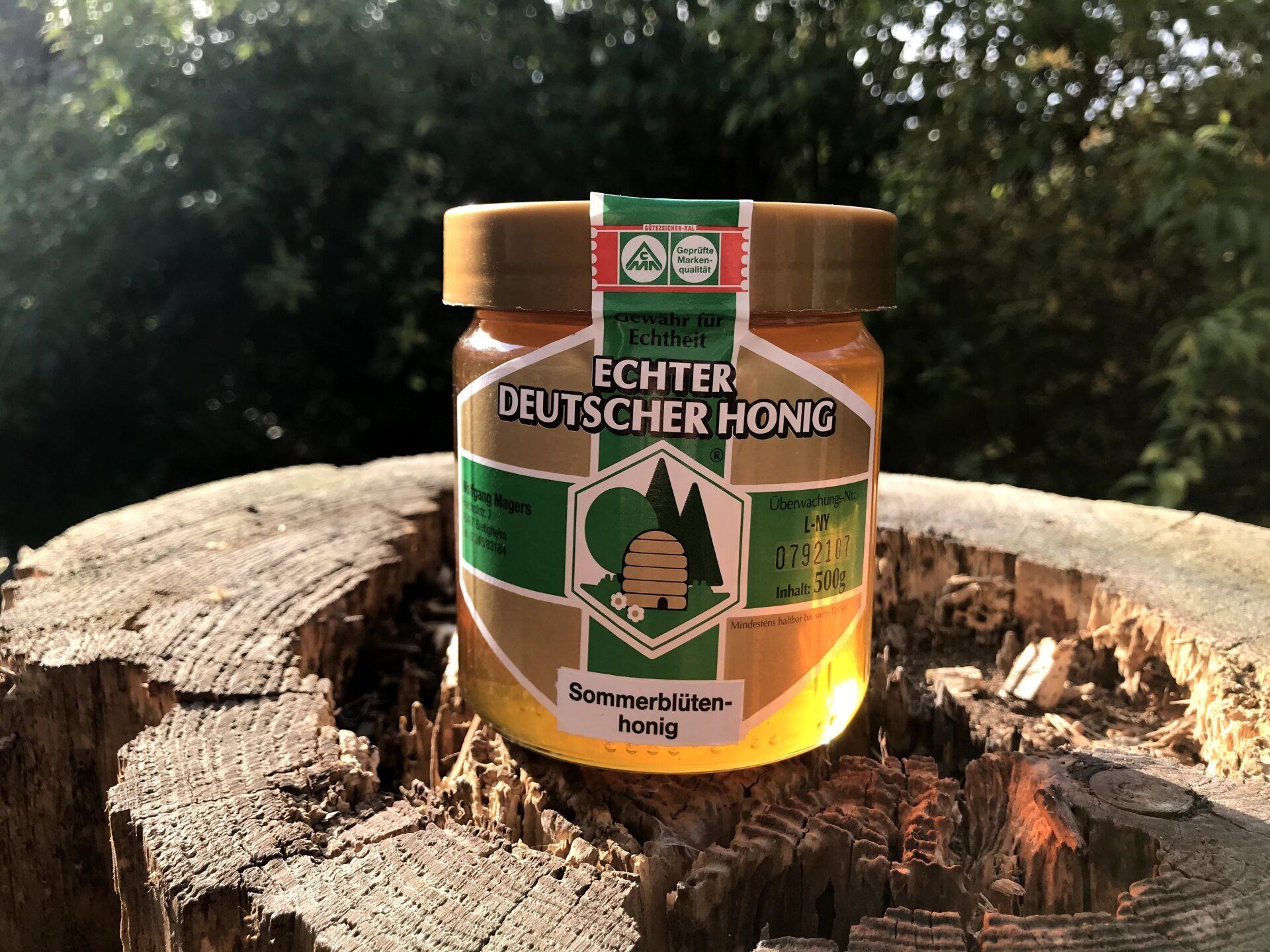 Ein DIB-Glas Sommerblütenhonig der Imkerei Magers aus dem Raum Rastatt/Karlsruhe auf einem Baumstumpf, im Hintergrund Bienenvölker