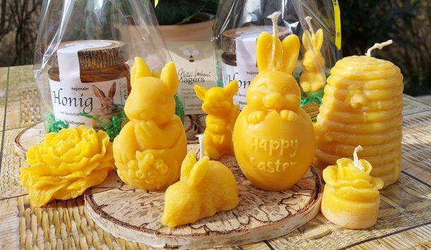Geschenke zu Ostern: Honig vom Imker und Bienenwachskerzen; Hasen-Figuren und weitere Kerzen vor 2 Geschenkpaketen mit Waldhonig
