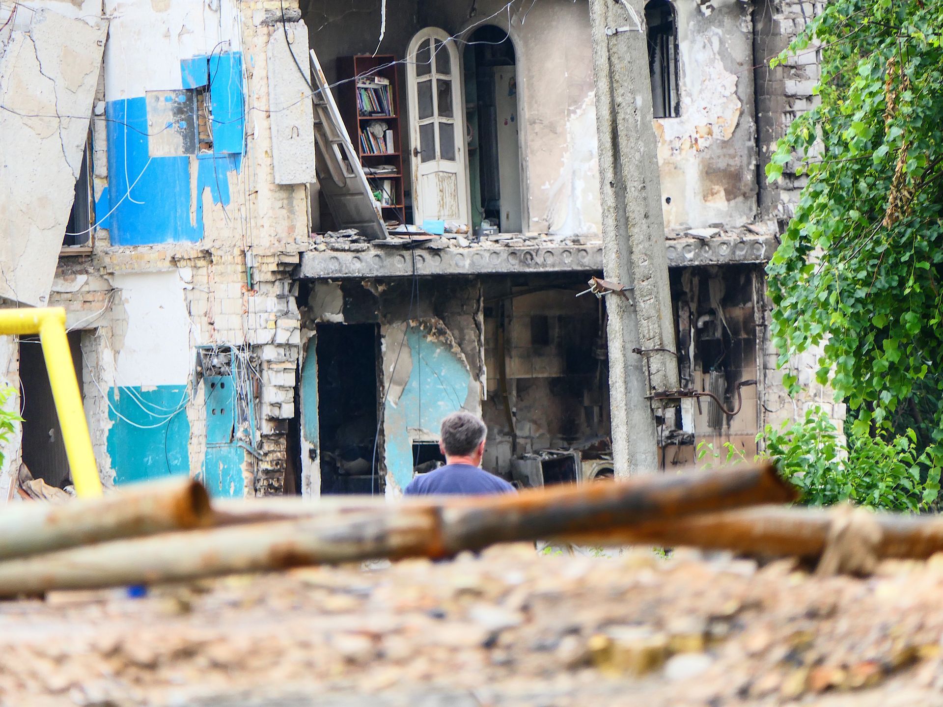 Destroyed apartment in Borodianka with exposed bookshelf and man in foreground, spring 2022