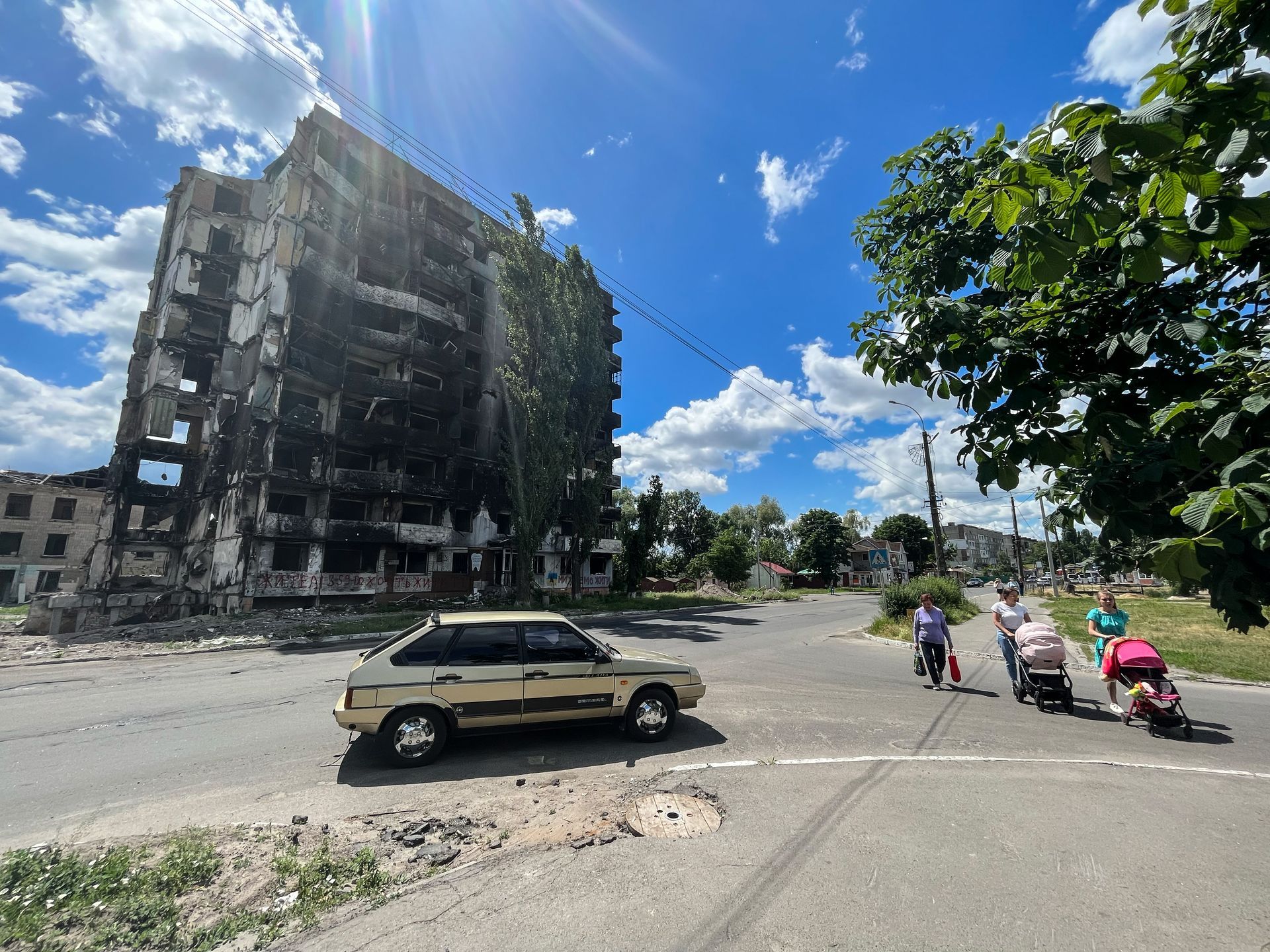 Destroyed apartment block in Borodianka, with families and children passing by, spring 2022