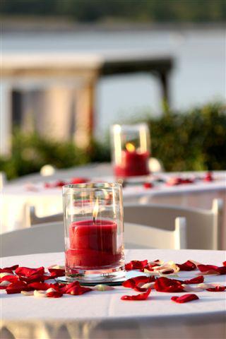 close up of red candle with red rose petals on white tablecloth