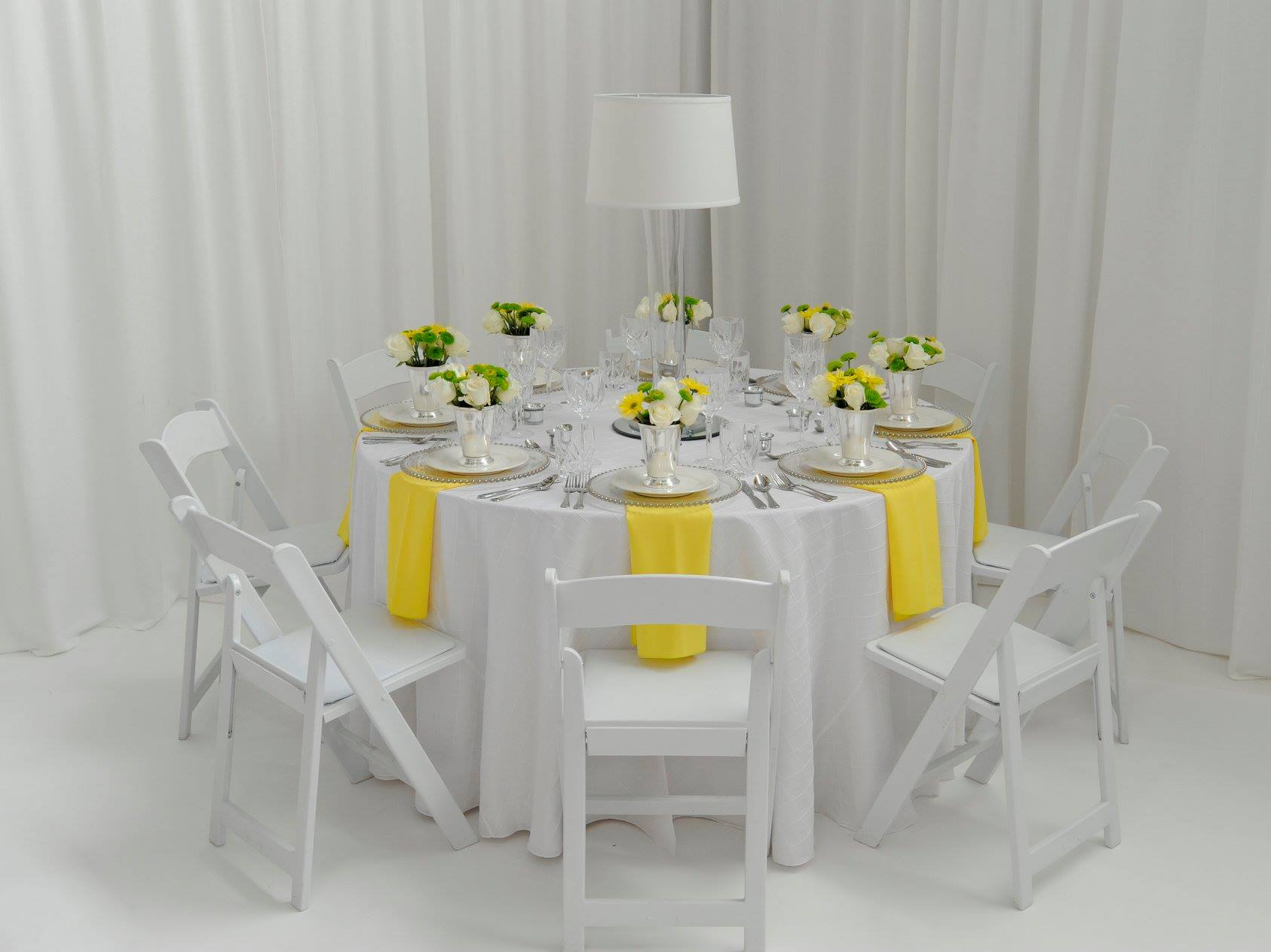 table arrangement with white chairs, yellow fabric accents, and yellow flowers