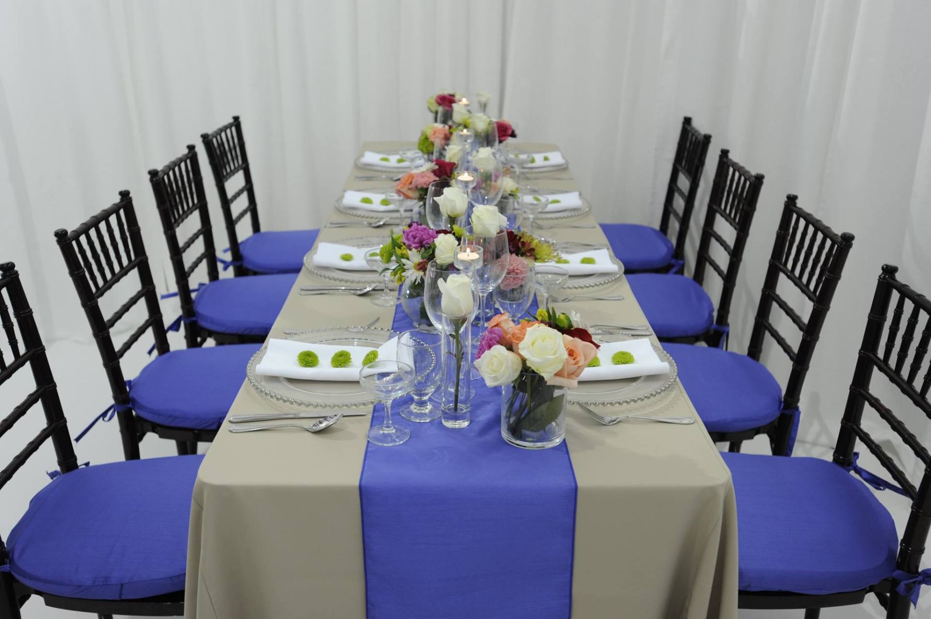 table arrangement concept with black Chiavari chairs with purple pads, tan runners, and multicolored floral arrangements