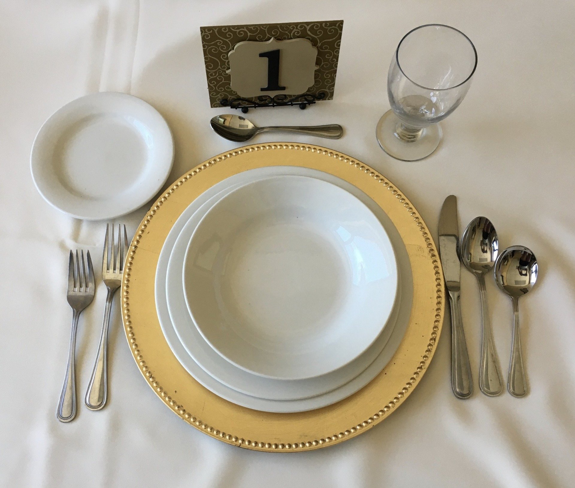 sample event place setting with flatware, glassware, dinnerware, charger, and table number