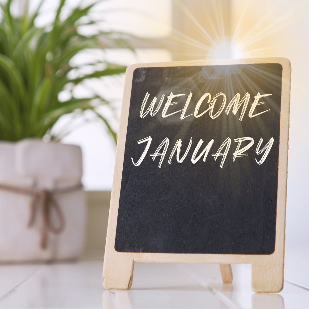 Bild mit einem Tisch, im Hintergrund eine Grünpflanze, eine Tafel mit einem Text: ,,Hallo Januar