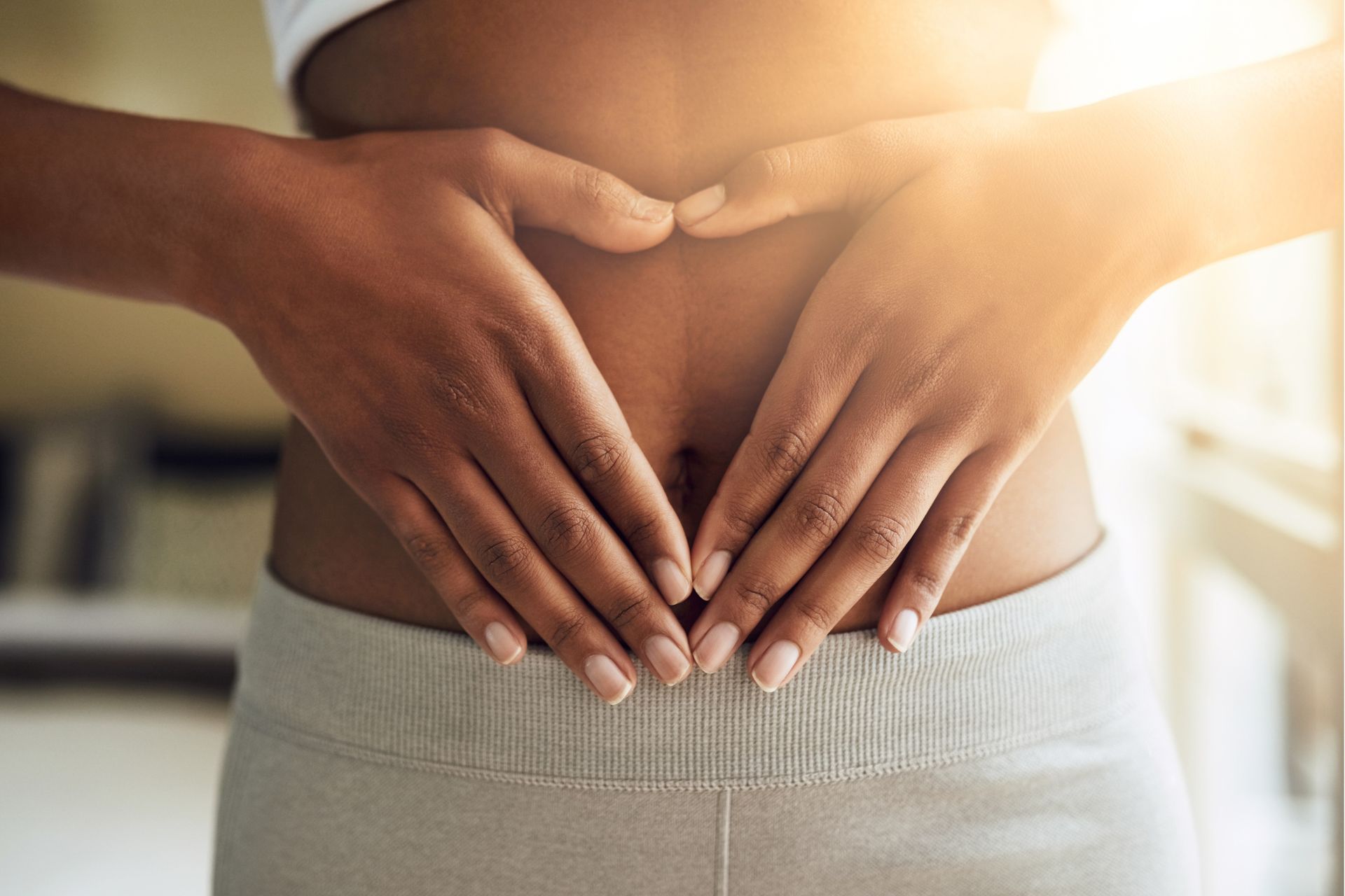 Bauch mit zwei, zu einem Herzen geformten, aufgelegten Händen