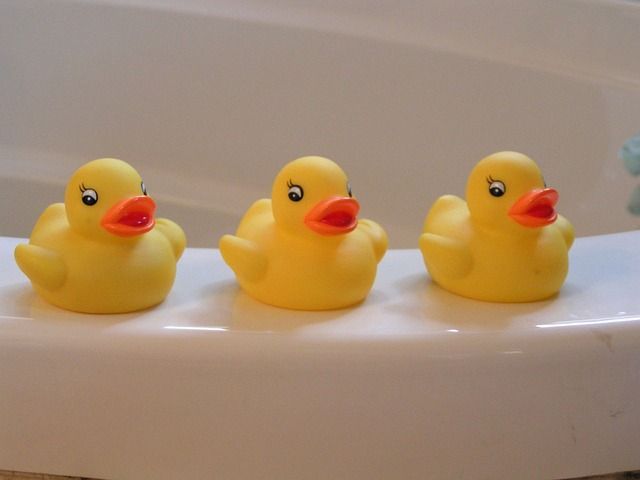 three rubber duckies on the edge of a tub