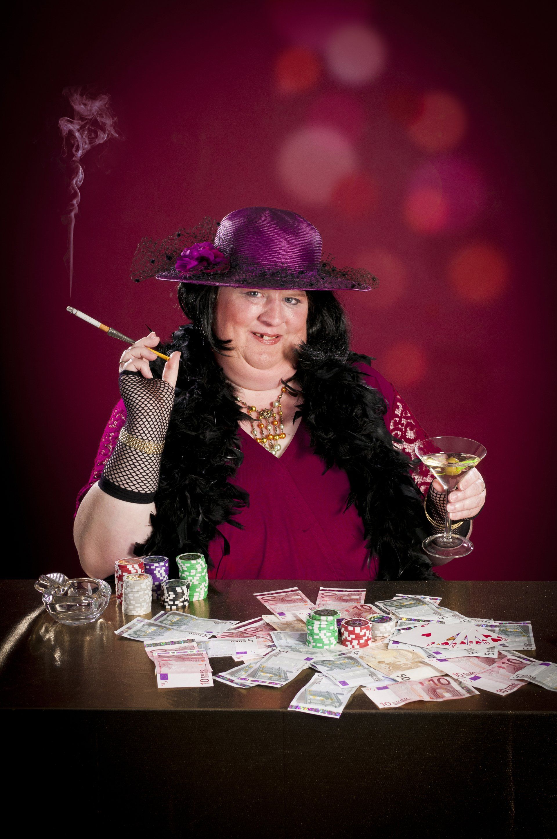 Auf dem Bild ist eine Frau mit Federboa, Hut, Handschuhen und einem Cocktail abgebildet.