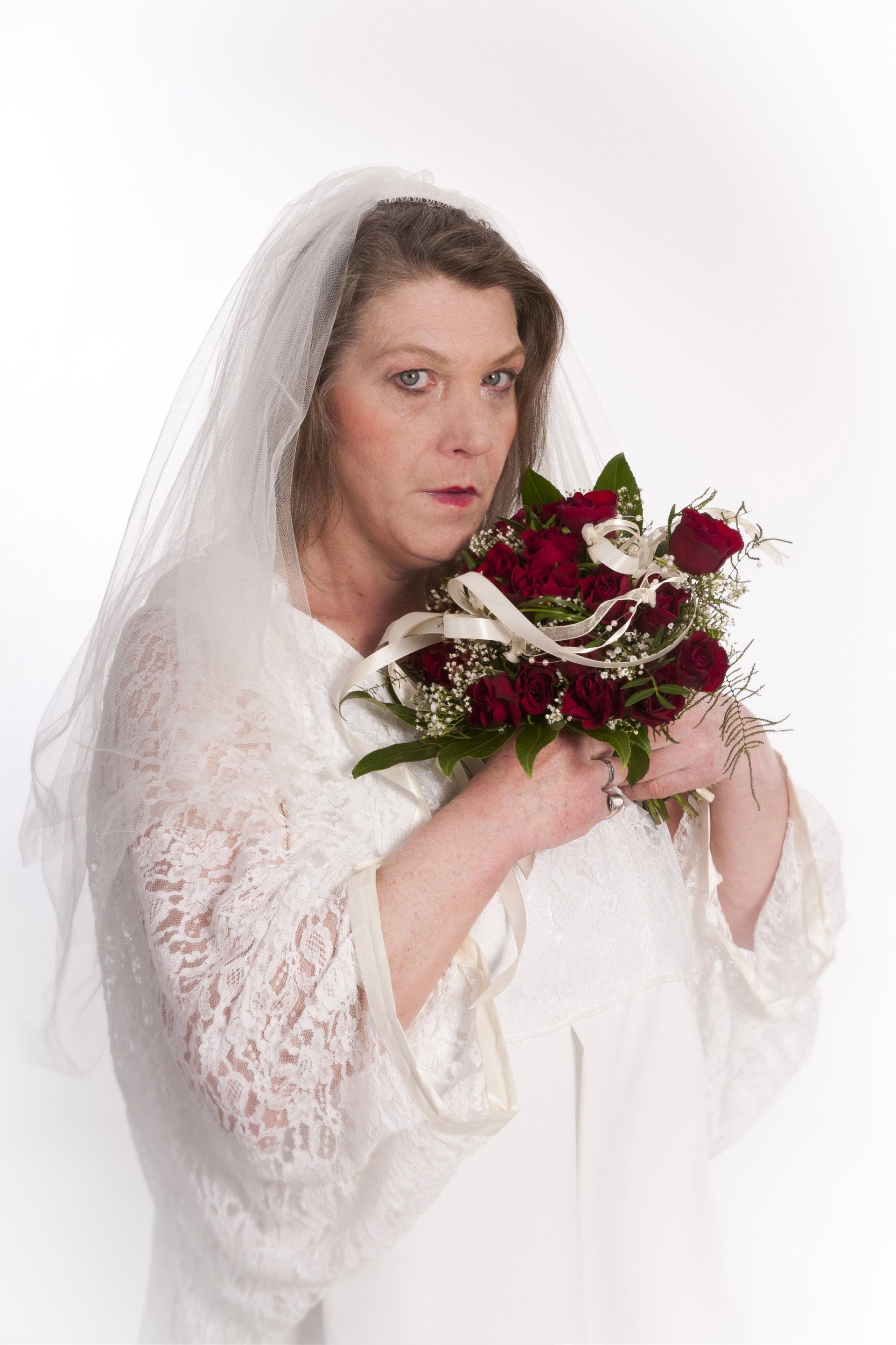 Die Frau auf dem Bild trägt ein Hochzeitskleid und hat einen roten Blumenstrauß in der Hand.