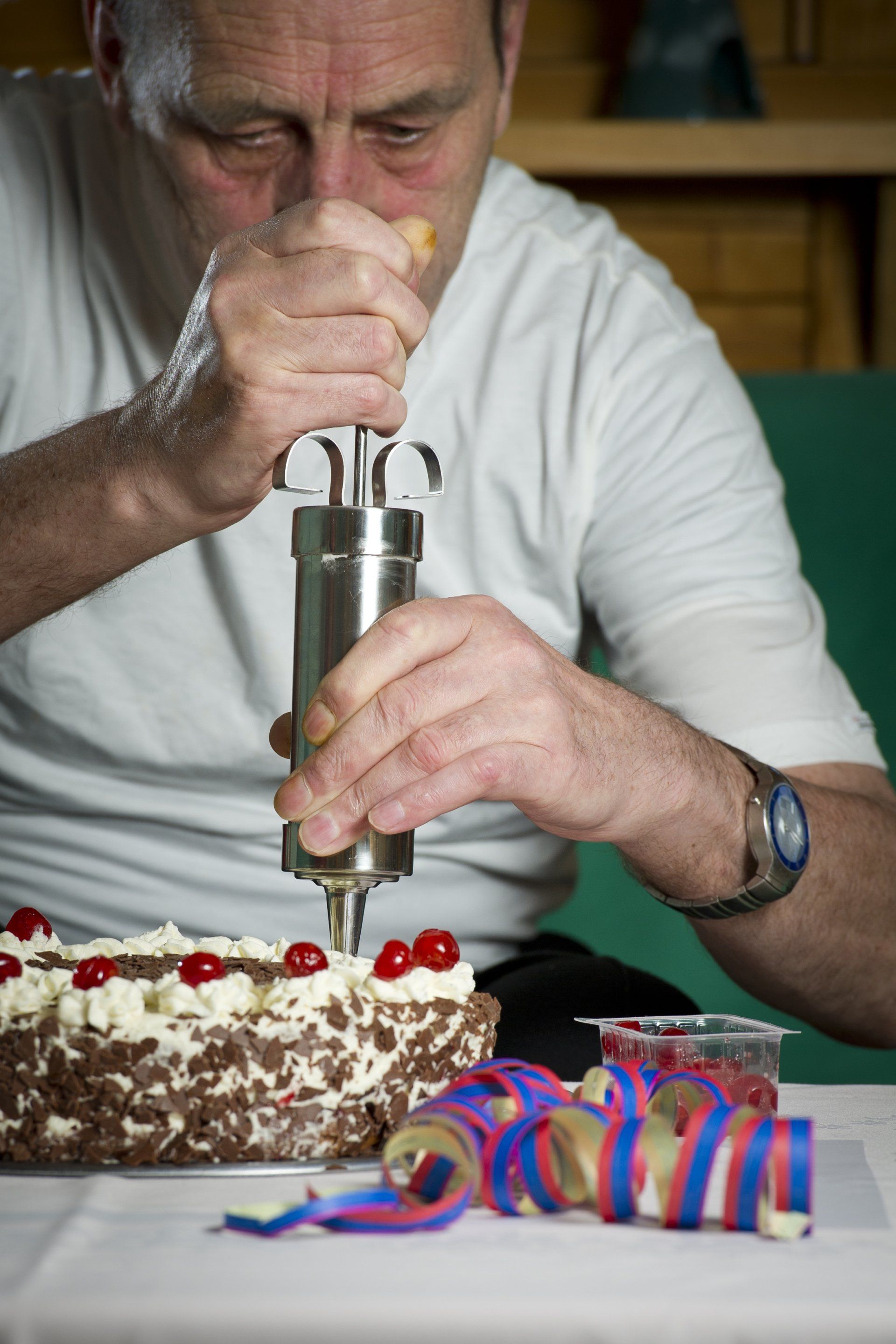 Auf diesem Bild ist Herr Martin zu sehen, dessen Traum es war, Konditor zu sein. Deshalb ist er hier dabei abgebildet, wie er gerade eine Schwarzwälder Kirsch Torte zubereitet. Er trägt für einen Konditor übliche weiße Kleidung, hält eine Garnierspritze in den Händen und neben der Torte befinden sich weitere Kirschen zum verzieren der Torte und bunte Luftschlangen.