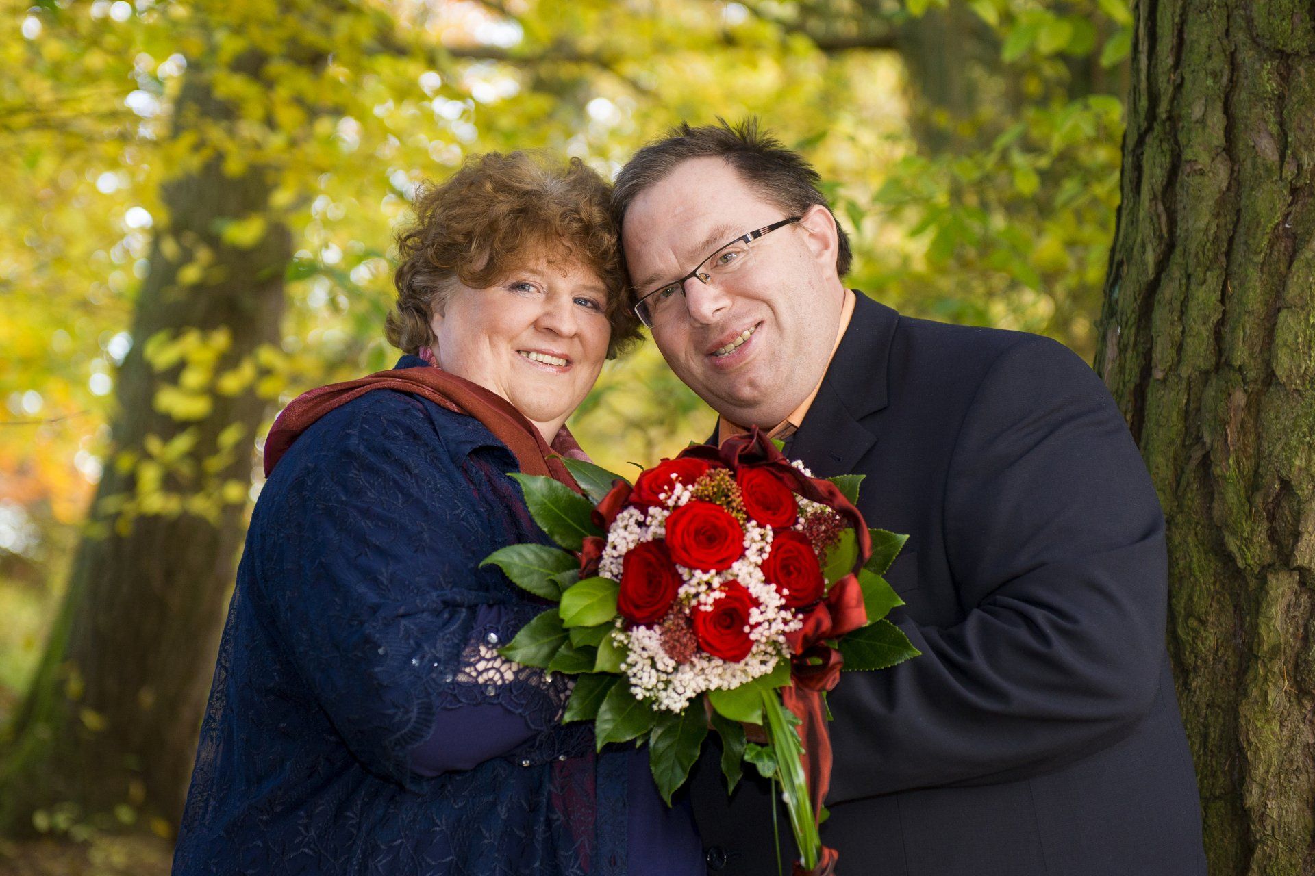 Auf diesem Bild stehen ein Mann und eine Frau eng zusammen. Sie halten gemeinsam einen Blumenstrauß.