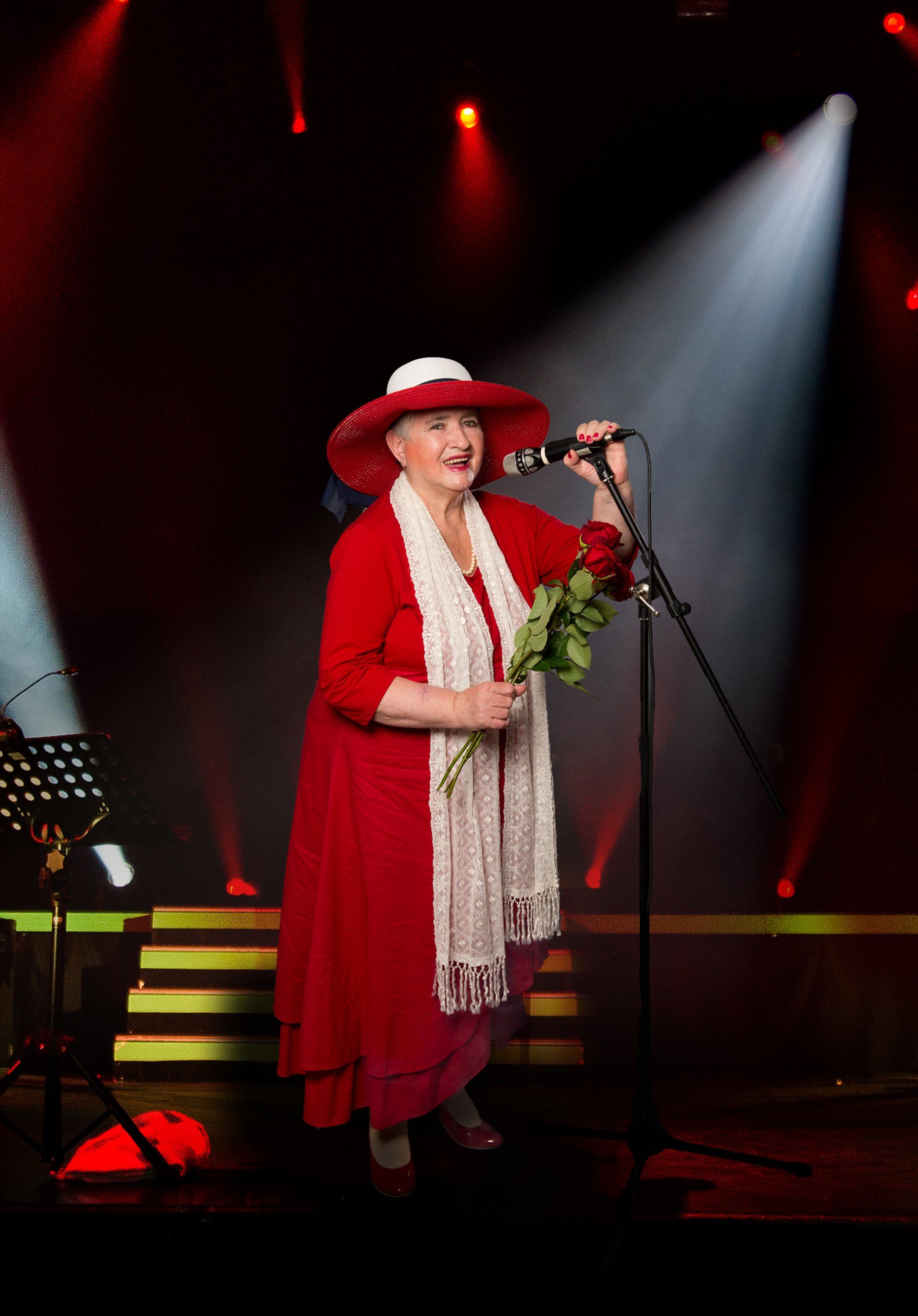 Auf diesem Bild ist Frau Ebenhoch zu sehen, die in ihrer Vergangenheit ein großer Schlager Fan war. Auf dem Foto steht sie auf einer Bühne und singt in ein Mikrofon vermutlich das Lied