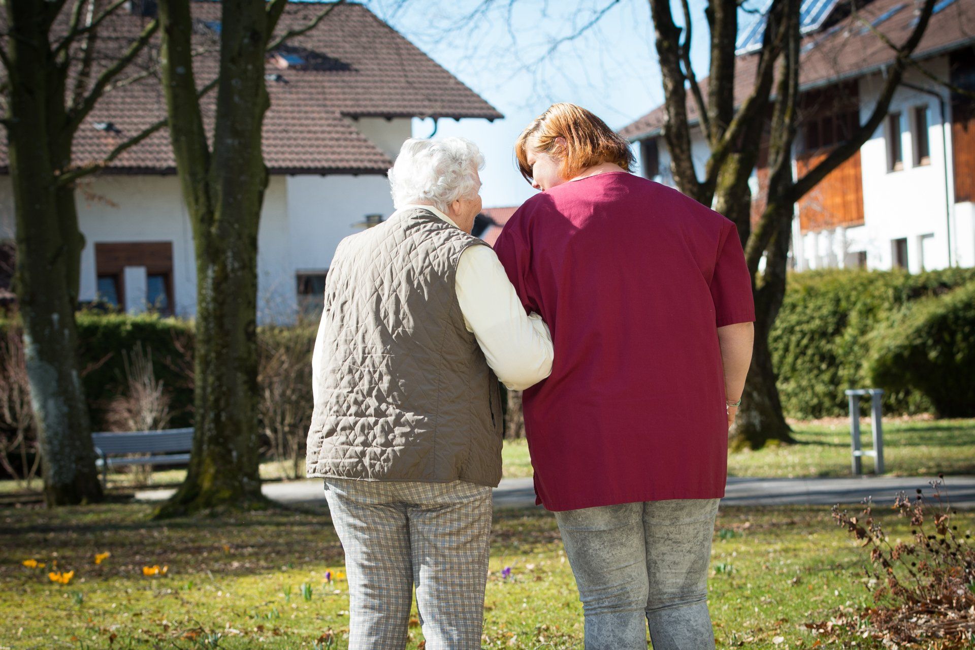 Auf diesem Foto sind zwei Frauen zu sehen, die Arm in Arm durch einen Garten laufen.