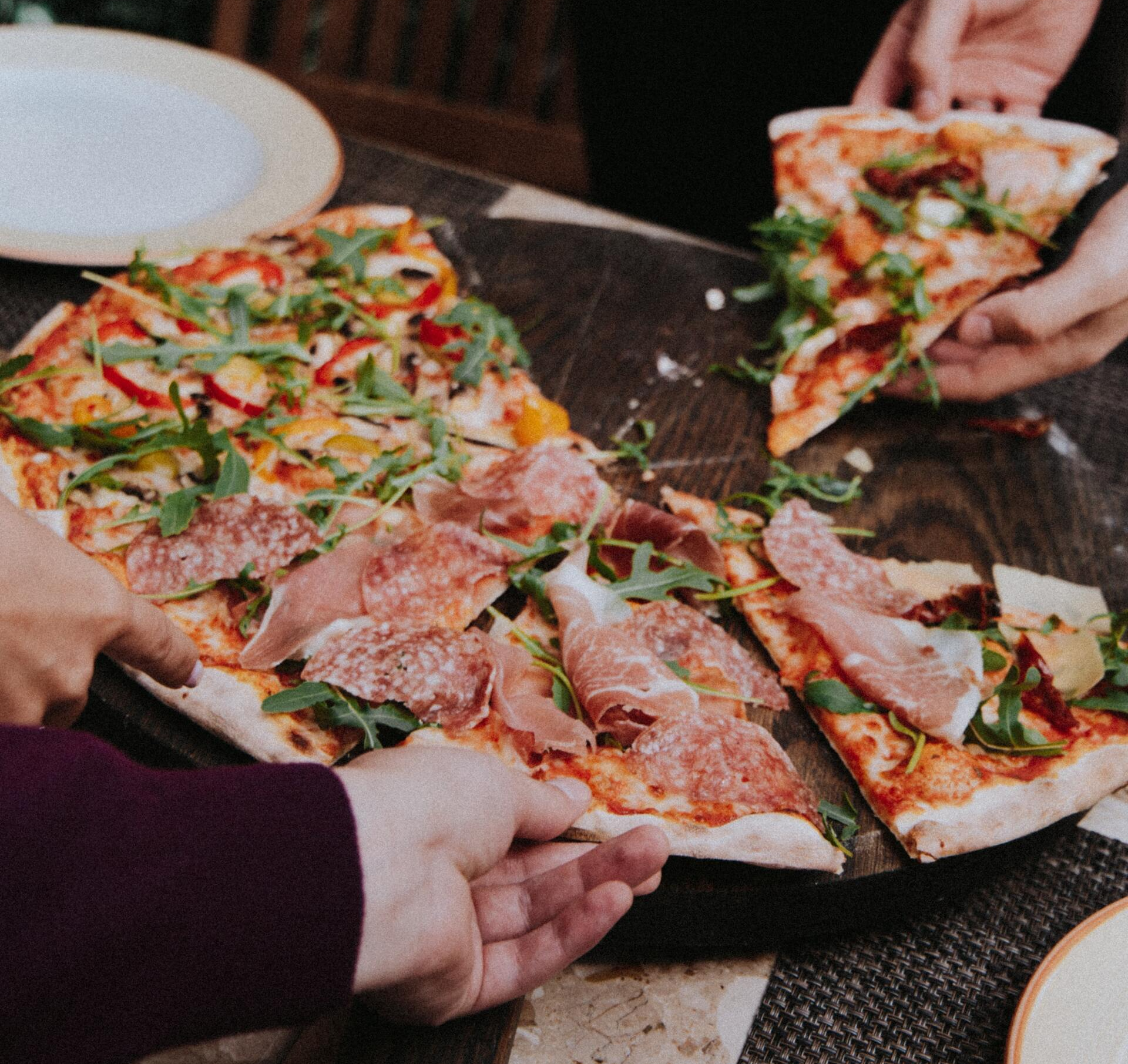 Auf diesem Bild sind Pizzastücke abgebildet, die sich verschiedene Menschen greifen.
