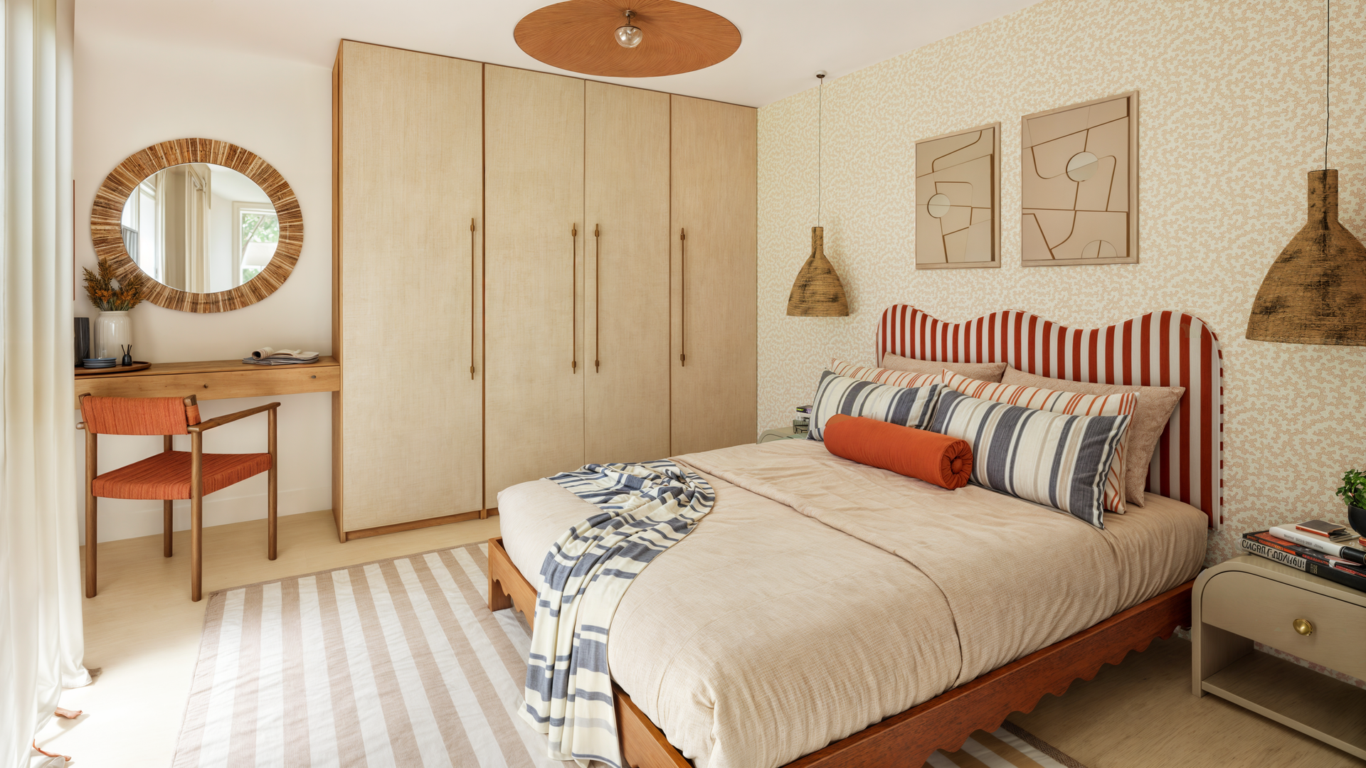 Une chambre avec une literie rayée rouge et blanche, un grand miroir, une chaise rayée orange et une commode.