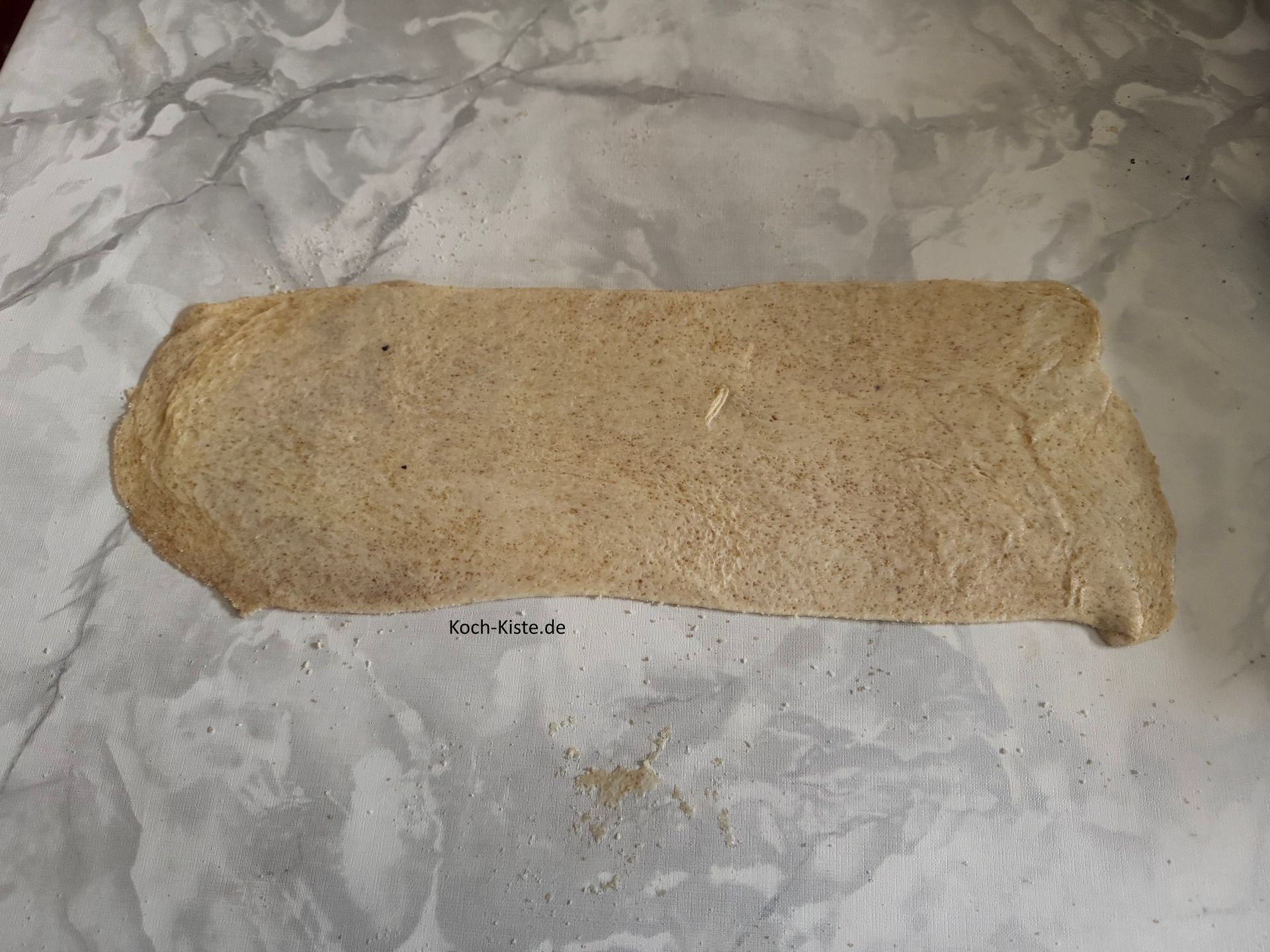 dann hebe den Teig an und drehe ihn um, so dass der Belag auf beiden Seiten verteilt wird. Nun rolle den Teig in rechteckiger Form aus.