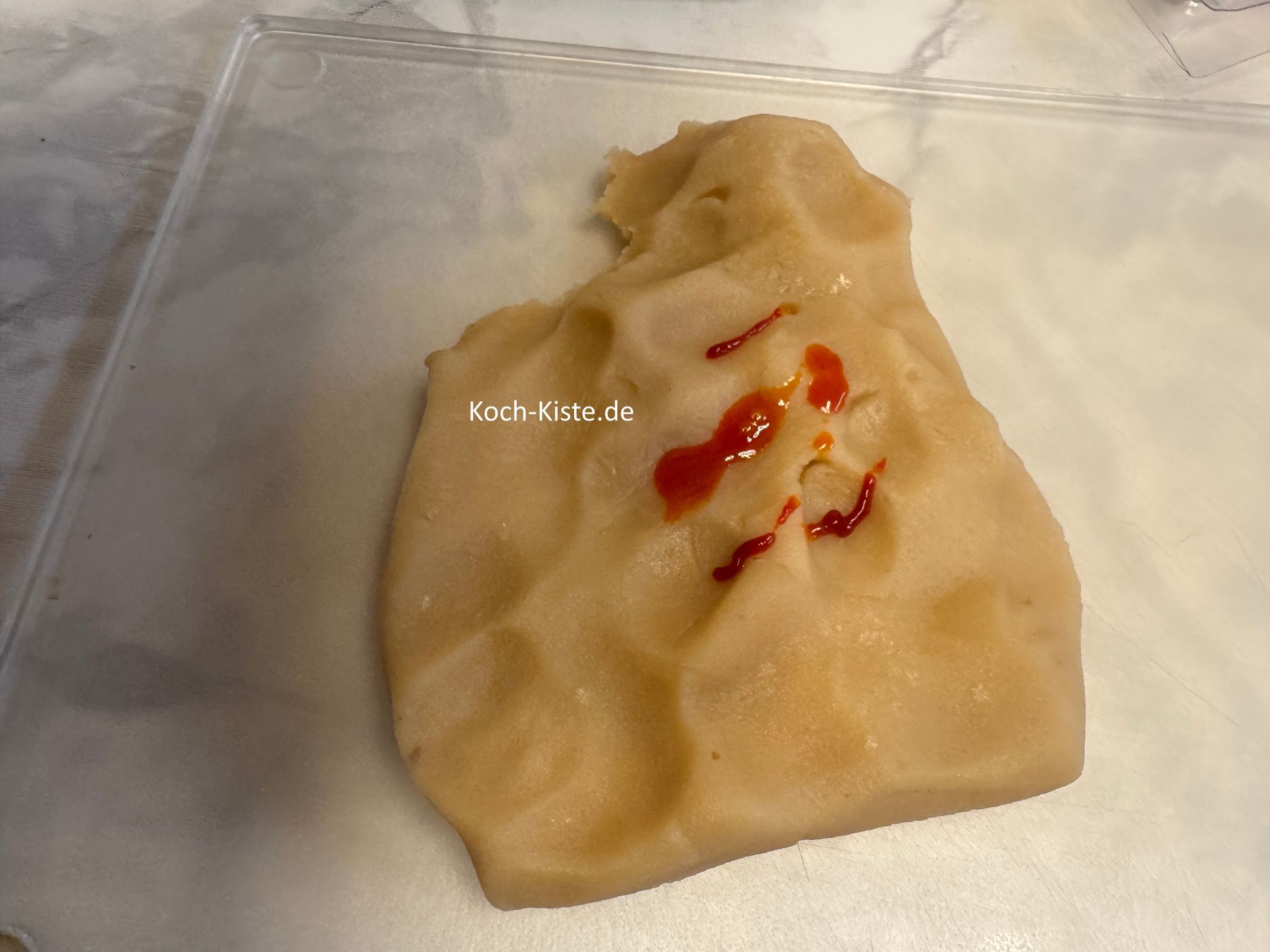 während der Backzeit kannst Du dich um die Dekoration kümmern. Dafür nimmst Du 200 g Marzipanrohmasse und legst sie auf das Schneidebrett. Obenauf kommt etwas orange Lebensmittelfarbe.