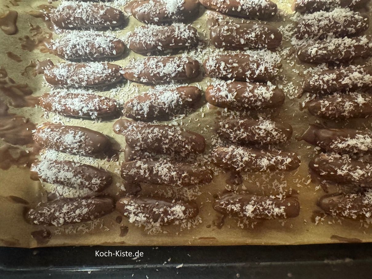 nehme Dir immer 1 Teigstange, bestreiche sie komplett mit Schokoladenglasur und lege sie auf das Backblech / Backpapier. Wenn Du 5 Teigstangen mit Schokoladenglasur bestrichen hast, bestreue sie mit Kokosflocken