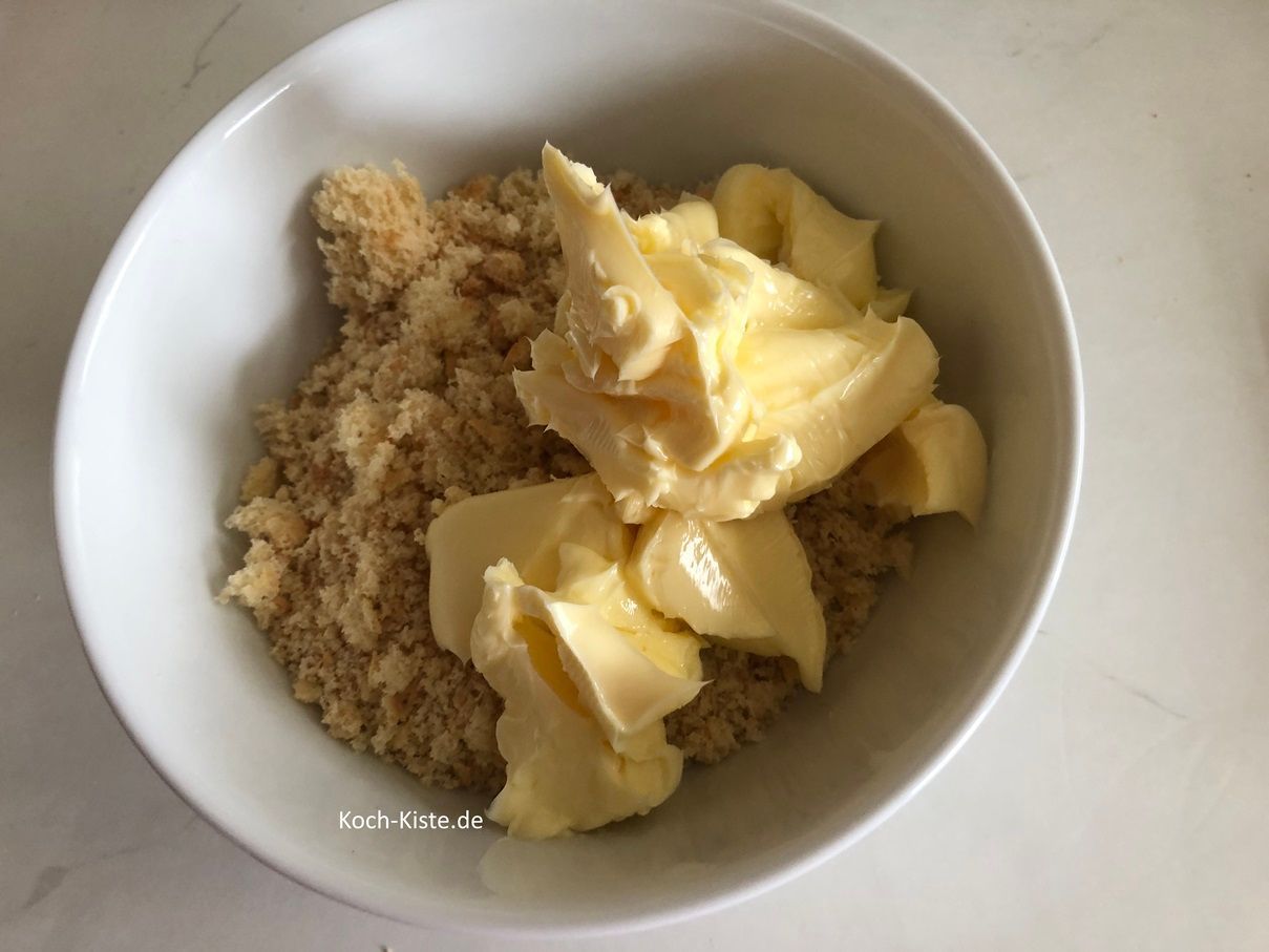 gebe die Biskuitlöffelkrümel in eine Schüssel und stelle sie auf die Küchenwaage auf 0, dann schubse mit dem Tafelmesser 100 g weiche Butter dazu