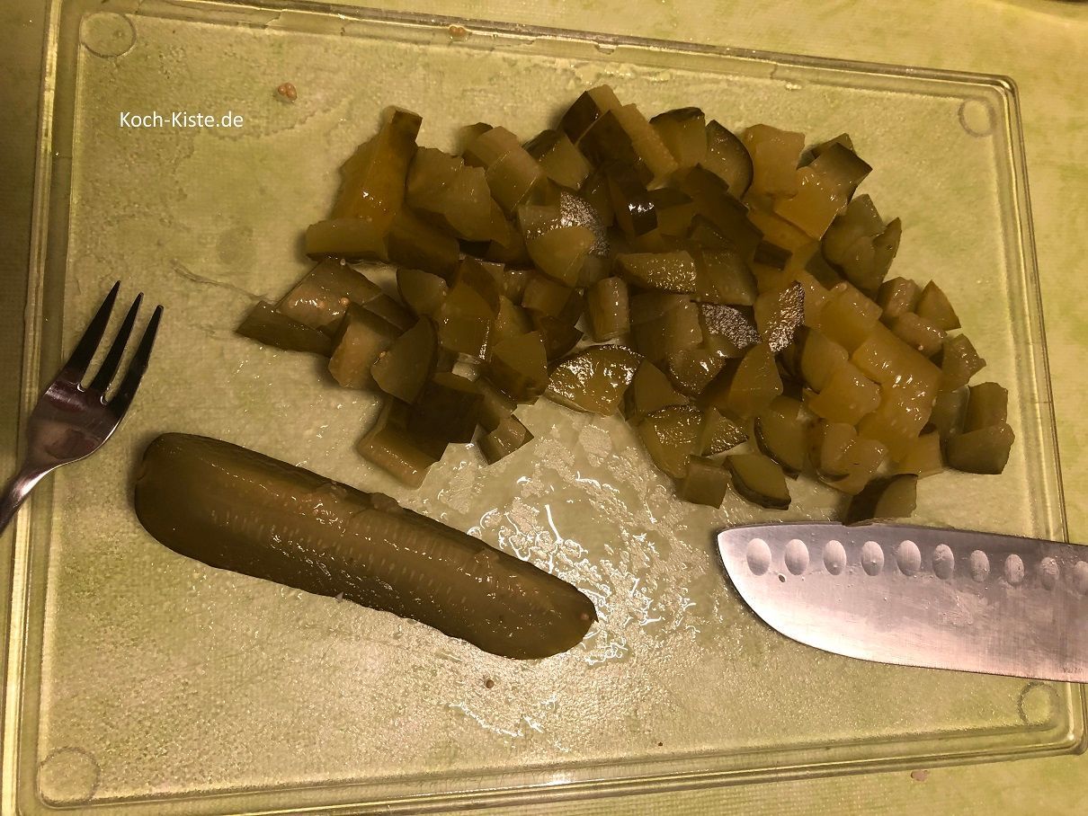 Gurkensticks aus dem Glas nehmen, auf das Schneidebrett legen und klein schneiden. Dann mit in die Salatschüssel geben
