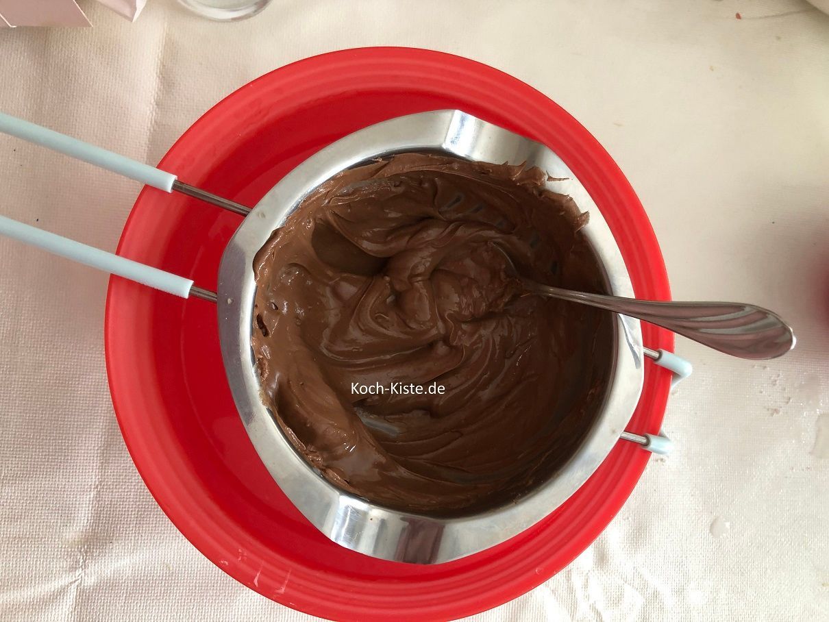 hänge die Schmelzschale in die Wasserschüssel. Nun gebe die Schokoladenglasur in die Schmelzschale und heißes Wasser in die Schüssel daunter . Mit den Teelöffel so lange rühren bis die Schokolade geschmolzen ist