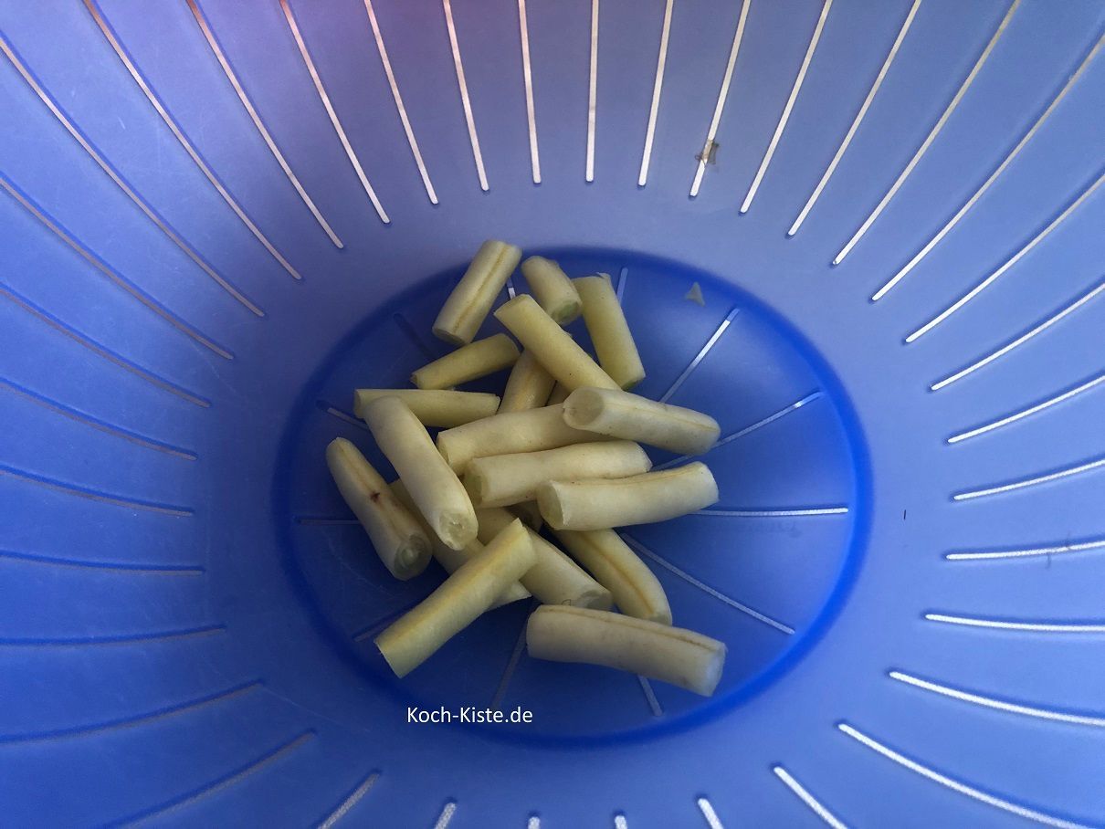 jetzt schneidest Du die Wachsbohnen direkt über dem Küchensieb in mundgerechte Stücke, so dass sie in das Küchensieb fallen