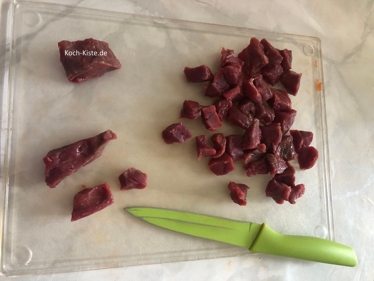 lege Dir die Gulaschstücke nacheinander auf das Schneidebrett und schneide sie in kleinere Stücke