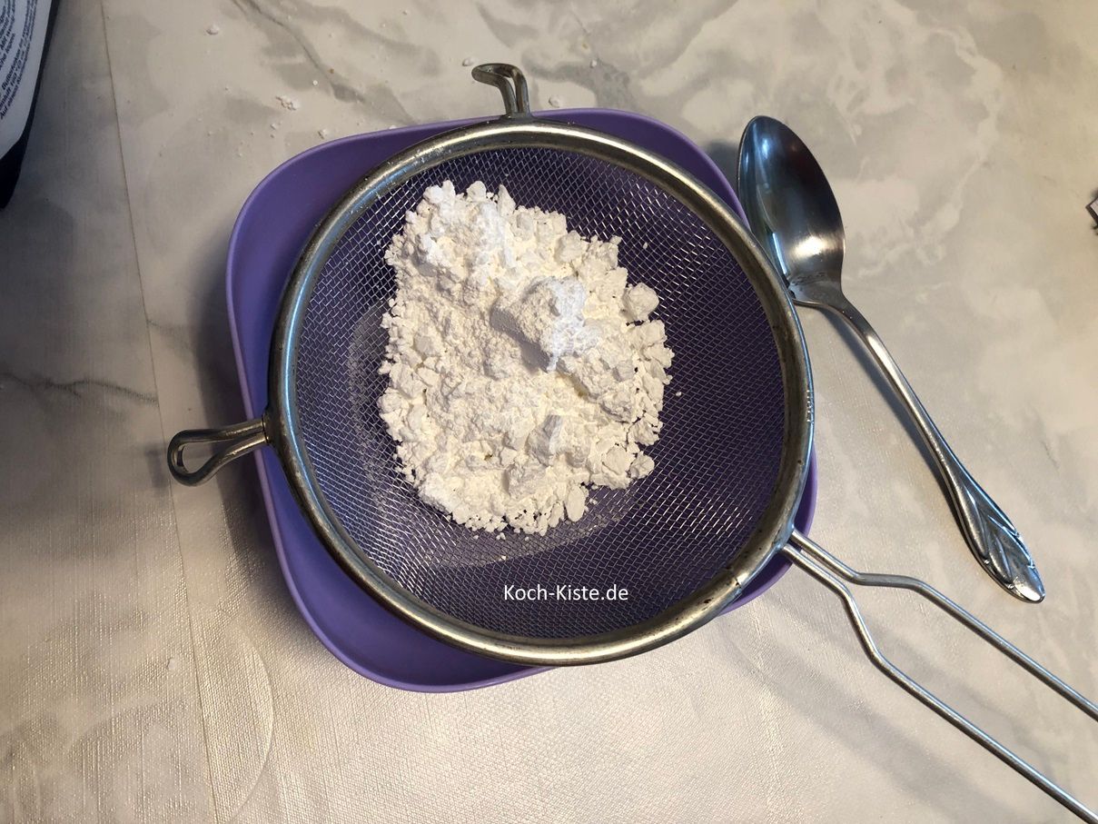 nehme dir eine kleine Schale und lege ein Passiersieb darauf. Nun gebe immer etwas von 250 Gramm Puderzucker und siebe ihn durch.