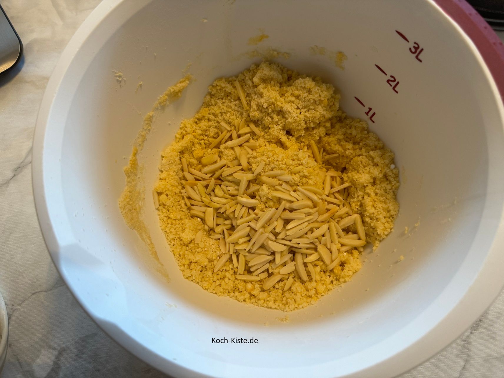 stelle die Rührschüssel erneut auf die Küchenwaage auf 0 und wiege 100 g blanchierte, Mandelstifte hinein. Verrühre alles mit dem 2 Esslöffel.