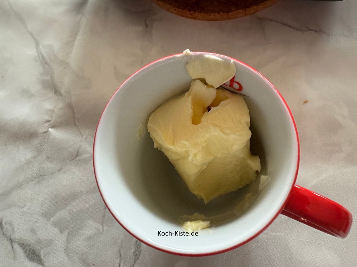 stelle den Kaffeebecher auf die Küchenwaage auf 0 und schubse mit dem Tafelmesser 125 g Butter hinein. Nun stelle den Kaffeebecher für ca. 30 Sekunden in die Mikrowelle um die Butter zu schmelzen. Achtung die Zeit kann abweichen, da die Mirkowellen unterschiedliche Wattleistungen haben.