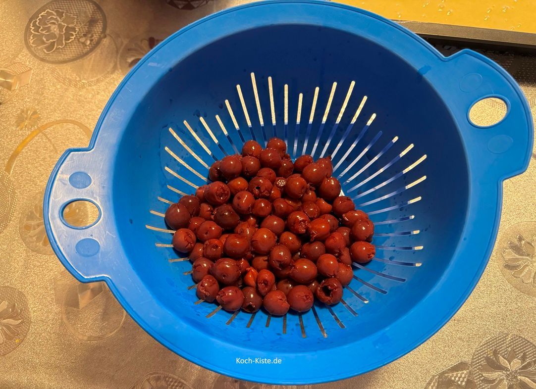 dann stelle das Küchensieb in die Küchenspüle, öffne das Kirschglas, kippe die Kirschen in das Küchensieb und lasse sie abtropfen. Dann stelle das Küchensieb auf einen kleinen Teller