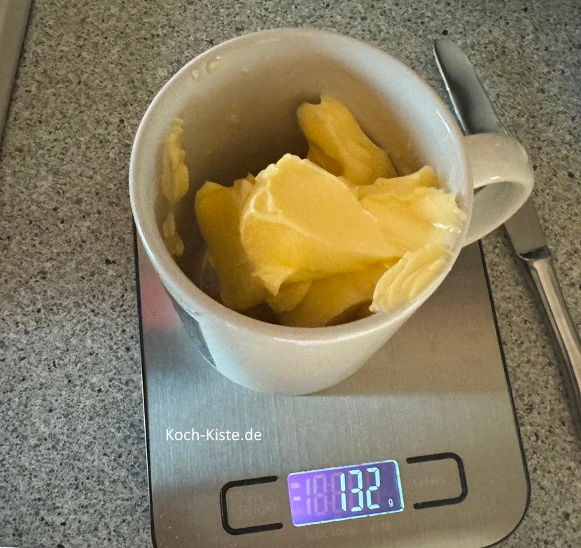 stelle einen Kaffeebecher auf die Küchenwaage auf 0 und schubse mit dem Tafelmesser 130 g Butter hinein. Stelle den Kaffeebecher in die Mikrowelle und lasse sie für ca. 30 Sekunden schmelzen. Achtung die Zeit kann abweichen, weil es viele verschiedene Wattleistungen bei den Mikrowellen gibt.
