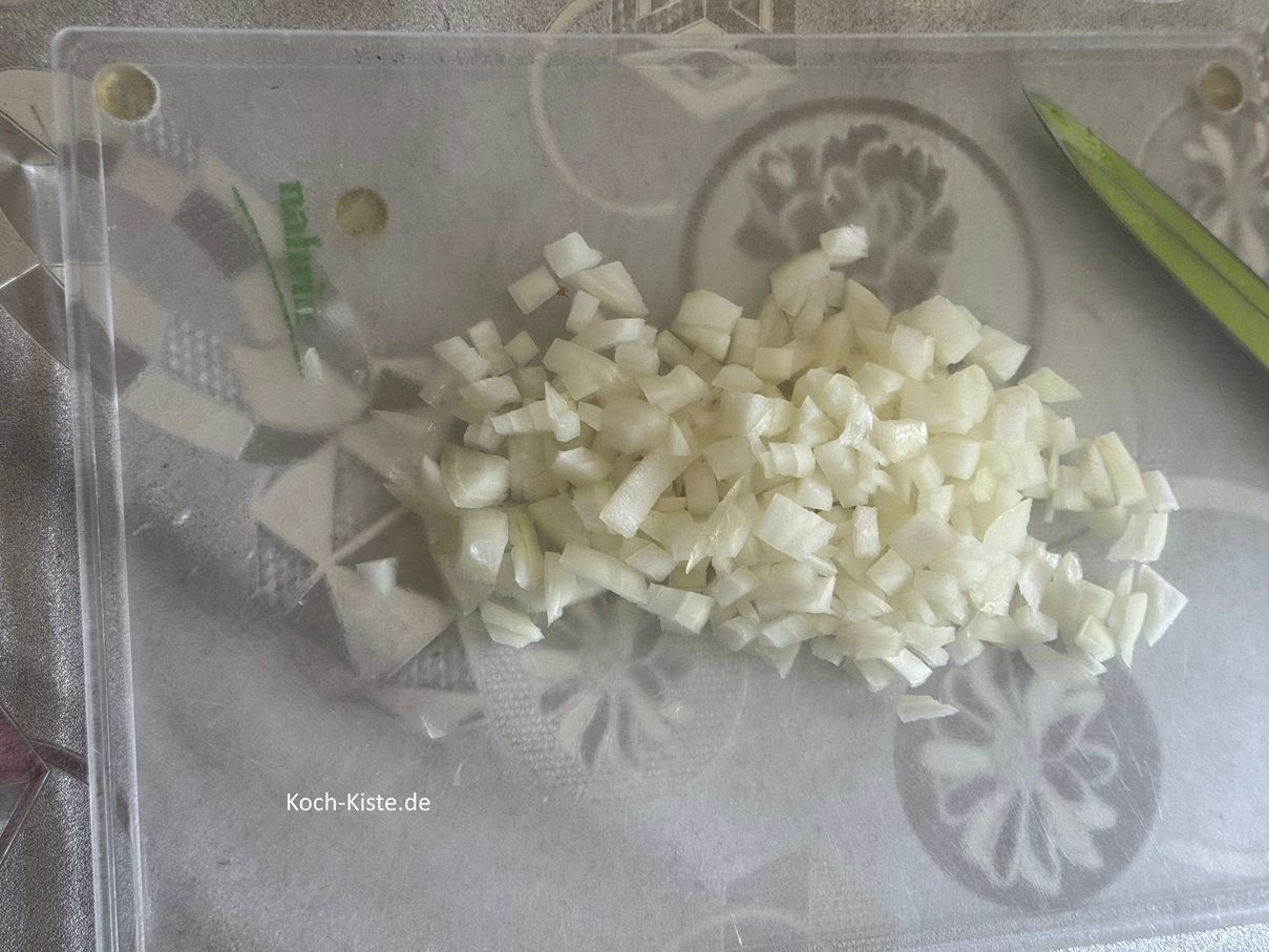 beginne damit die Zwiebel auf das Schneidebrett zu legen und oben und unten ein Stück zu entfernen. Dann kannst Du die Zwiebel pellen. Lege die Zwiebel wieder auf das Schneidebrett und schneide sie in Scheiben. Als nächstes entferne den Zwiebelkern, schneide die Zwiebel in Streifen und dann in kleine Stücke.
