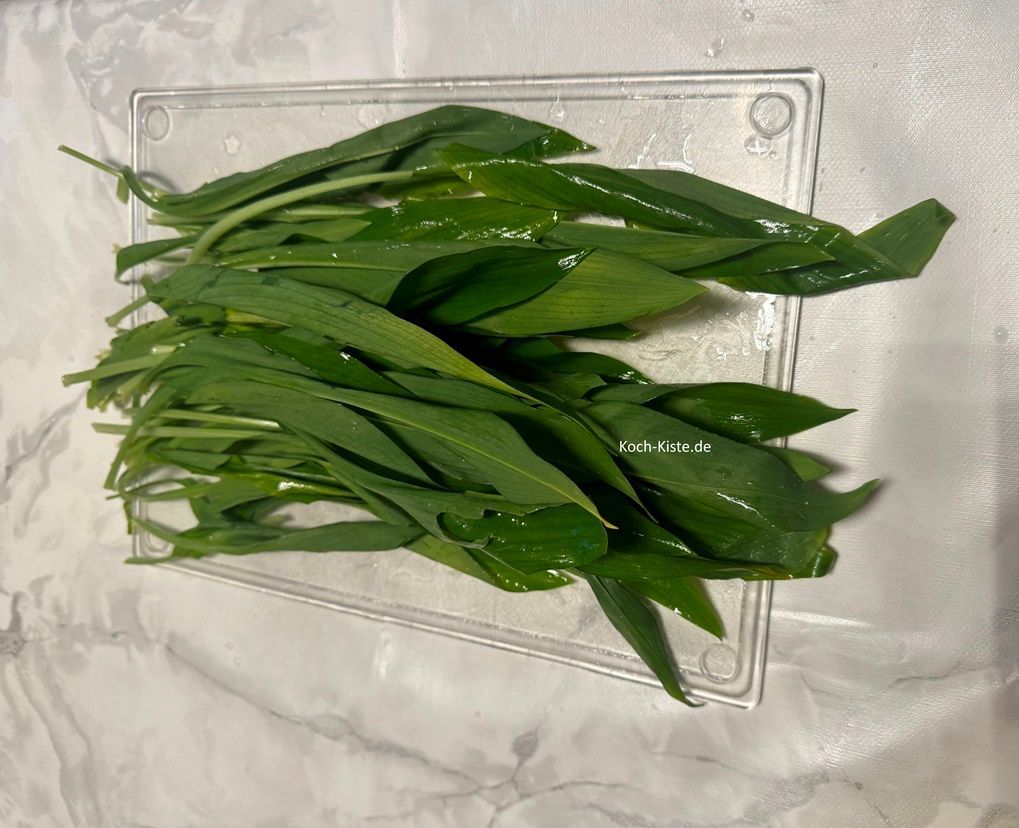 beginne damit den Bärlauch unter kaltem, fließendem Wasser abzupüen und trocken zu schütteln. Dann lege ihn auf die Arbeitsfläche und entferne die Stiele. Die Blätter legst Du auf das Schneidebrett.
