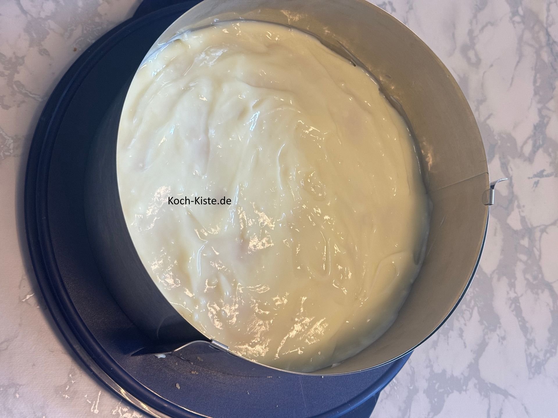 lege um den Tortenboden einen Tortenring, rühre mit einem Esslöffel den Pudding noch mal um und gebe ihn dann auf den Tortenboden.