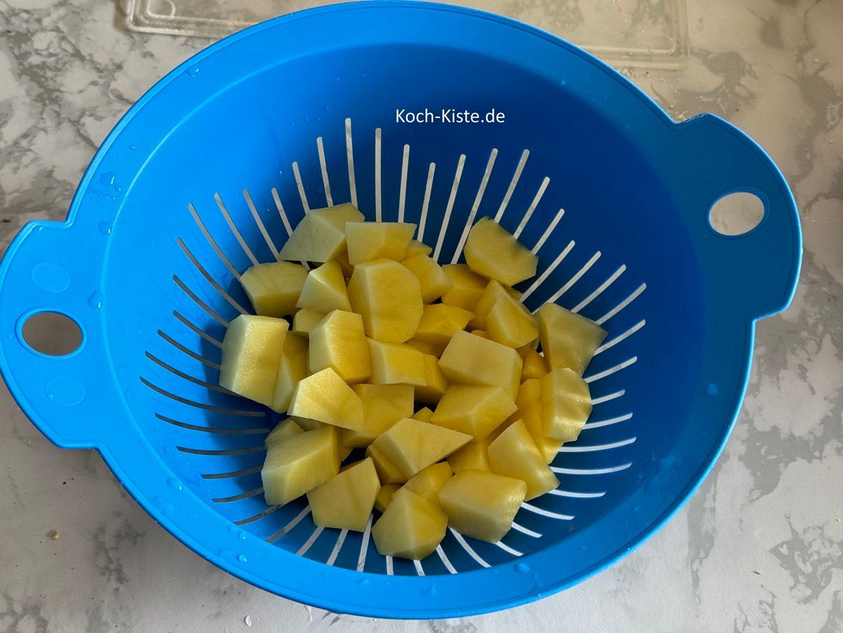 Beginne damit die Kartoffeln zu schälen un in ein Küchensieb zu legen. Spüle die Kartoffeln unter kaltem. fließendem Wasser ab und lasse sie abtropfen. Als nächstes lege die Kartoffeln nacheinander auf das Schneidebrett, halbiere sie , viertel sie und schneide sie in Stücke. Die Kartoffelstücke gebe wieder in das Küchensieb.